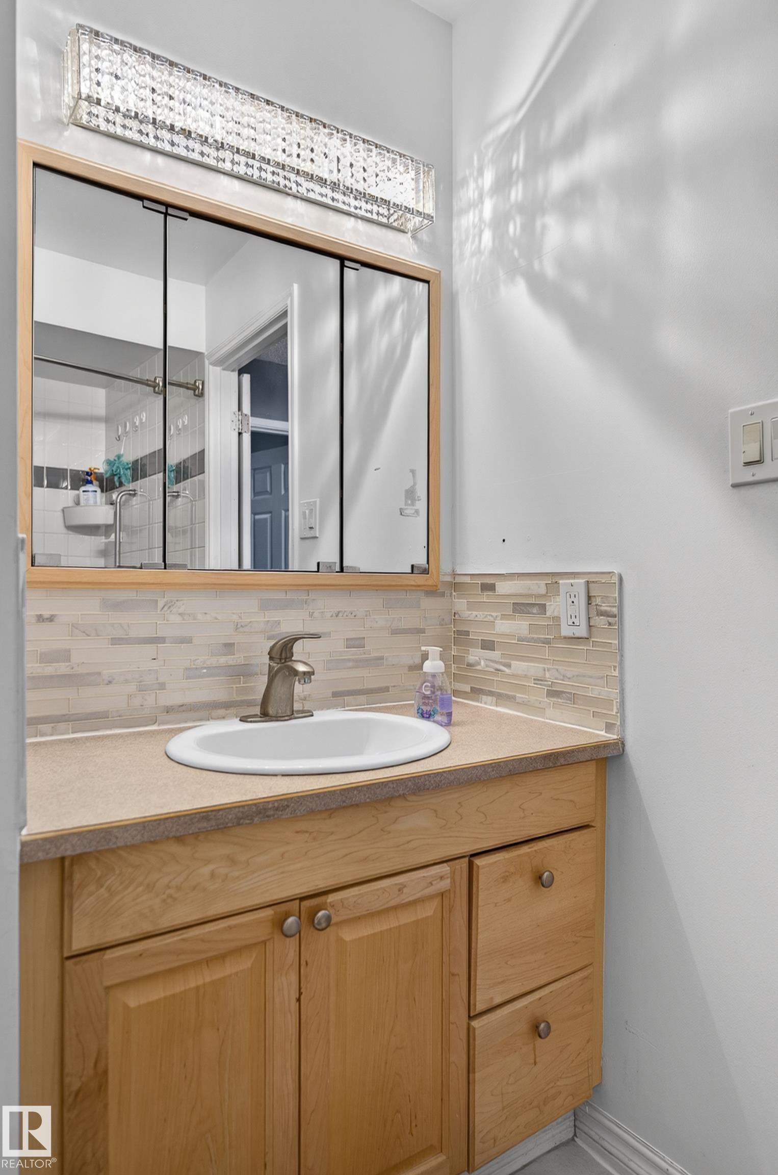 Vanity featuring a light wood-finish cabinet with double doors and two drawers, a rectangular undermount sink, and a brushed nickel faucet - 13445 40 Street Nw, Edmonton, AB