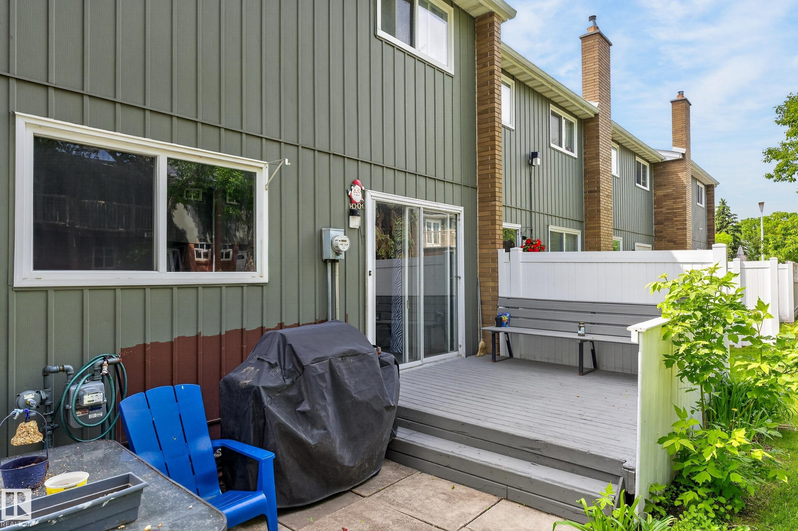 Rear exterior featuring a gray deck with built-in bench seating, white vinyl privacy fencing, and sliding glass door access - 13445 40 Street Nw, Edmonton, AB