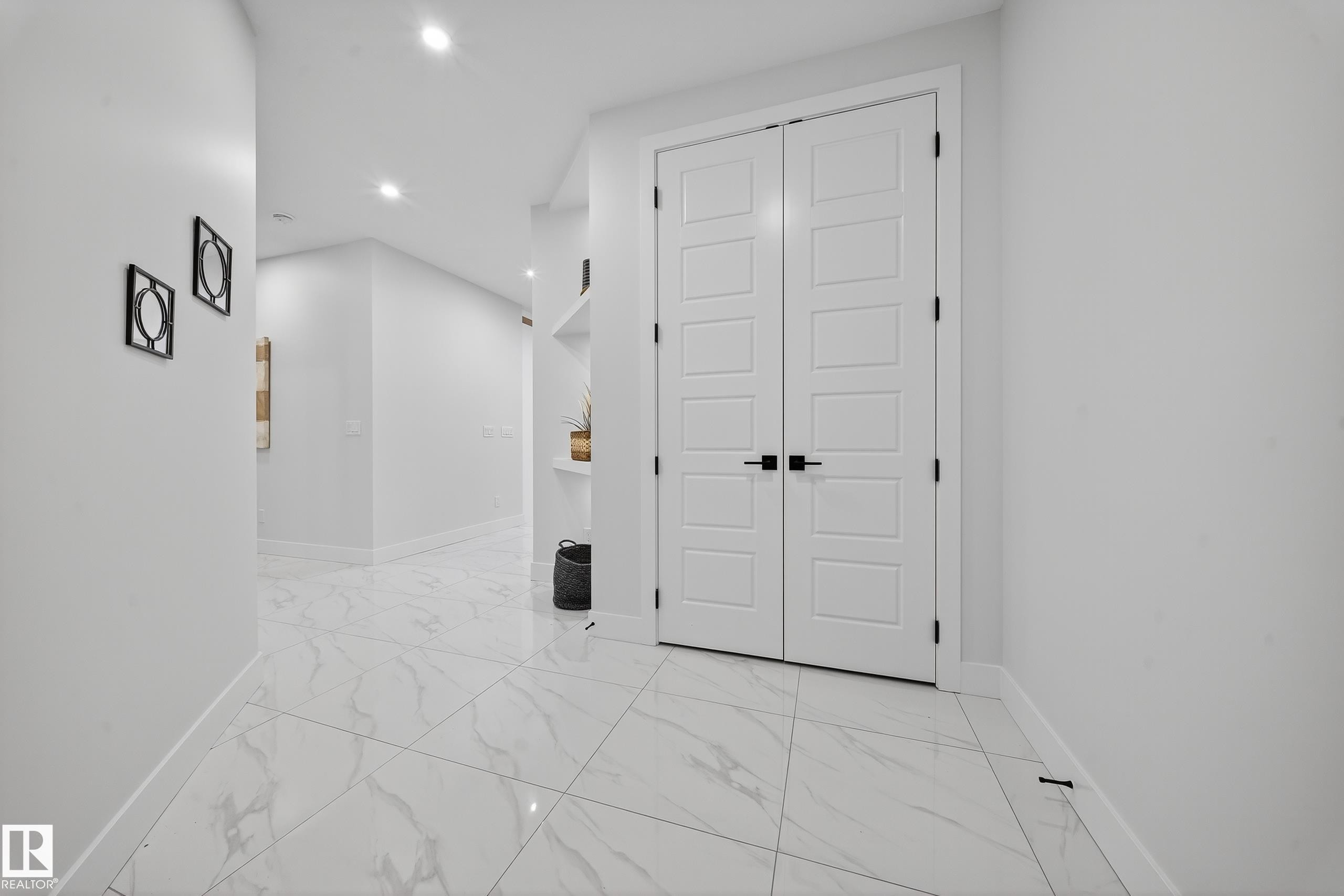 Double panel doors with black hardware, recessed lighting, white walls, and large format white tile flooring with gray veining - 372 Creekside Green, Leduc, AB