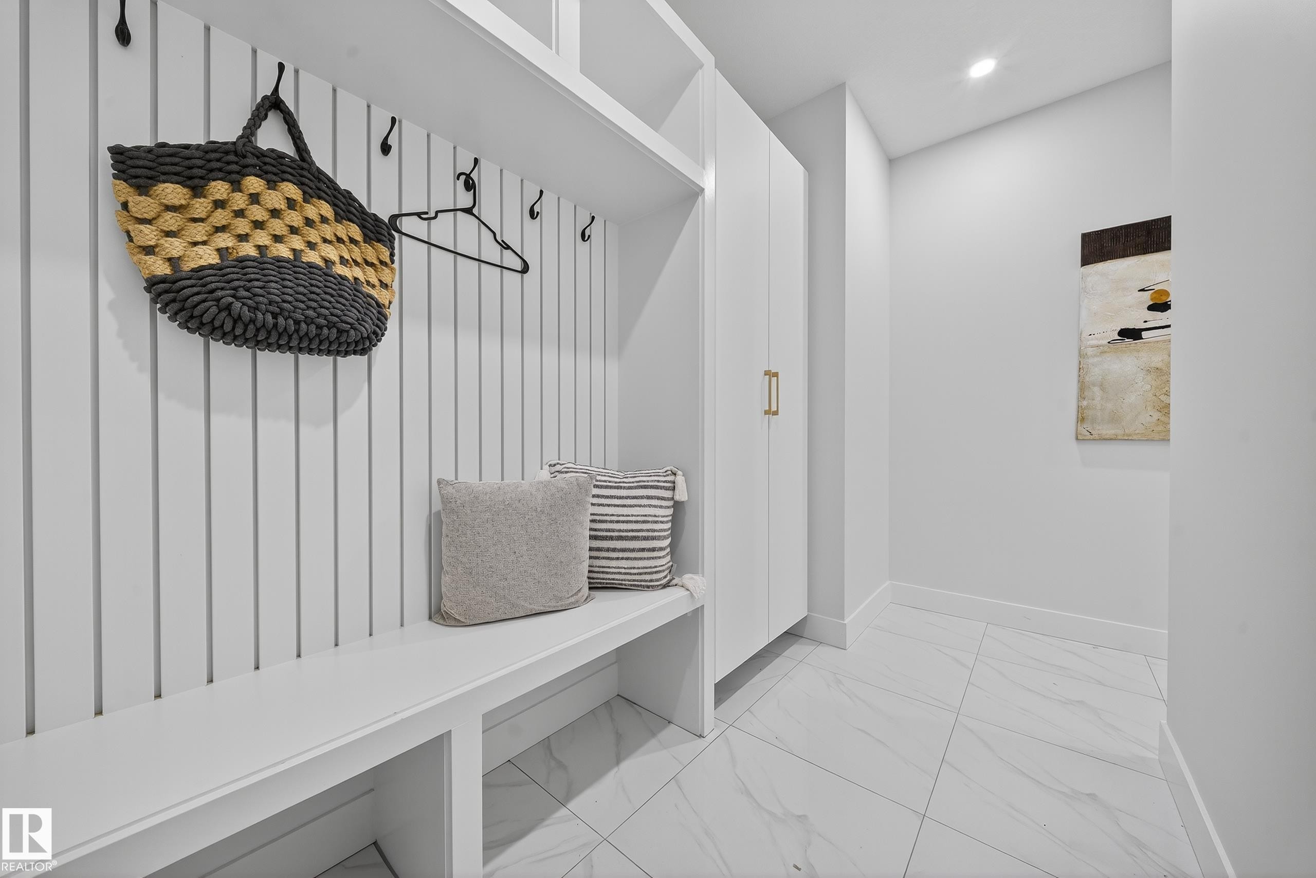 Built-in white mudroom bench with cubby storage, vertical slat wall paneling, and integrated hooks - 372 Creekside Green, Leduc, AB