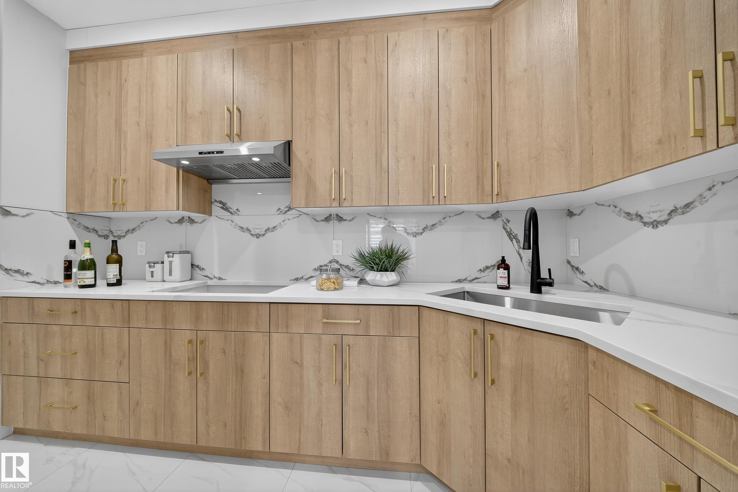 Modern kitchen featuring wood-finish cabinetry with gold-tone hardware, white countertops, and a white backsplash with gray veining - 372 Creekside Green, Leduc, AB