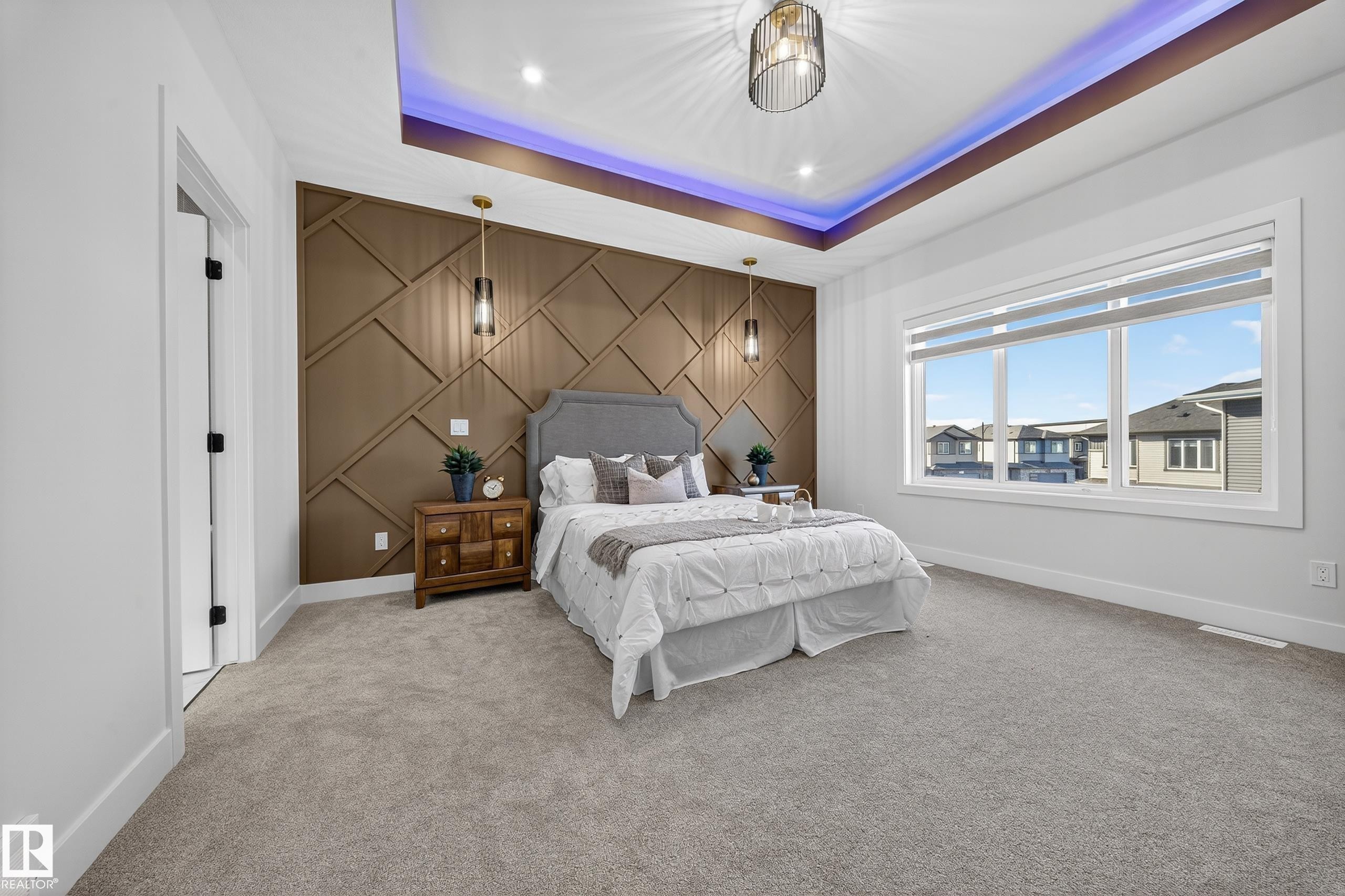 Spacious room featuring a decorative accent wall, tray ceiling with recessed lighting, and large windows - 372 Creekside Green, Leduc, AB