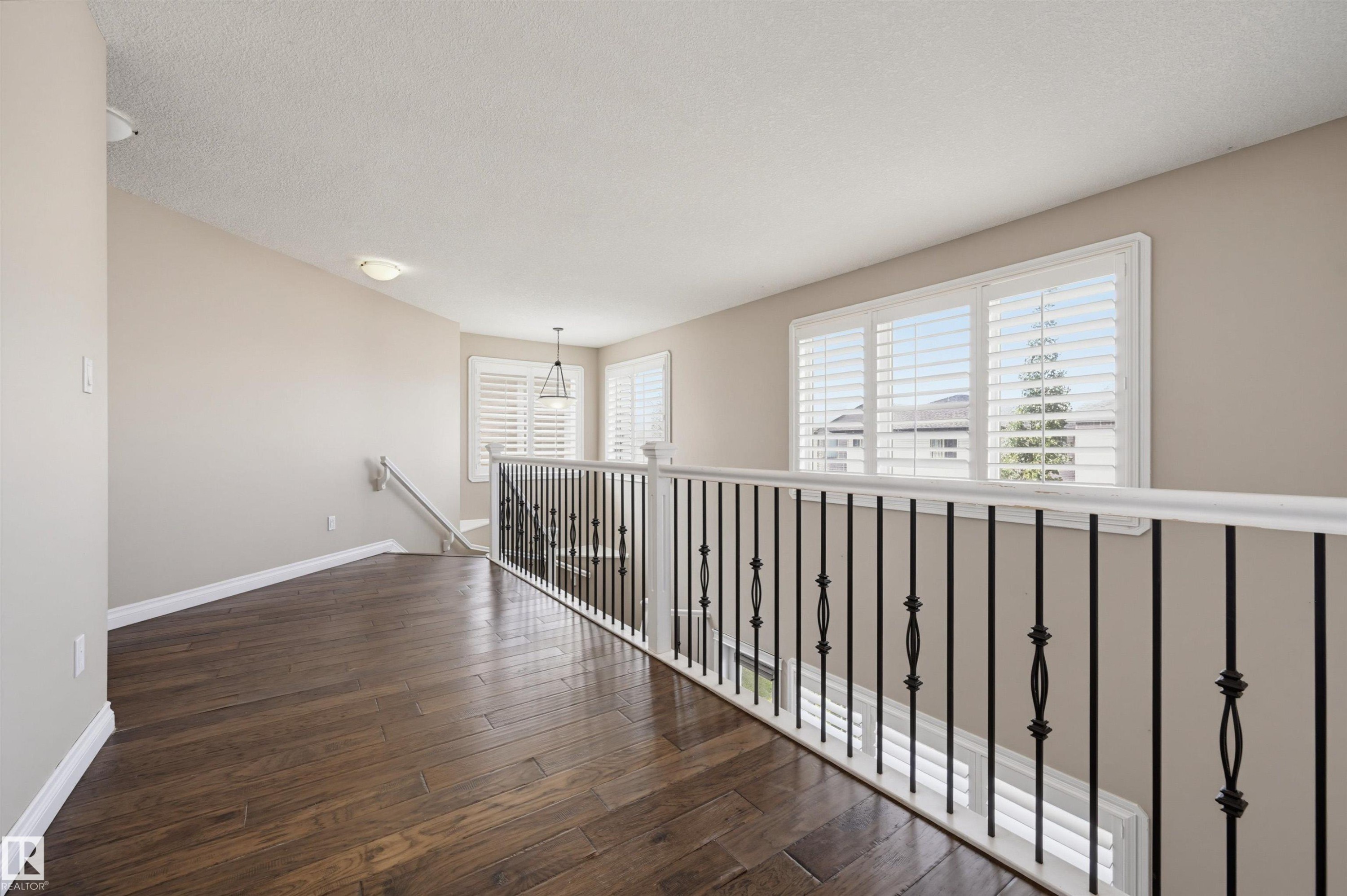 Upper-level landing featuring wood-finish flooring, a white and wrought iron railing, and multiple windows with white plantation shutters - 21928 97 Avenue Nw, Edmonton, AB - Indoor Photo Showing Other Room