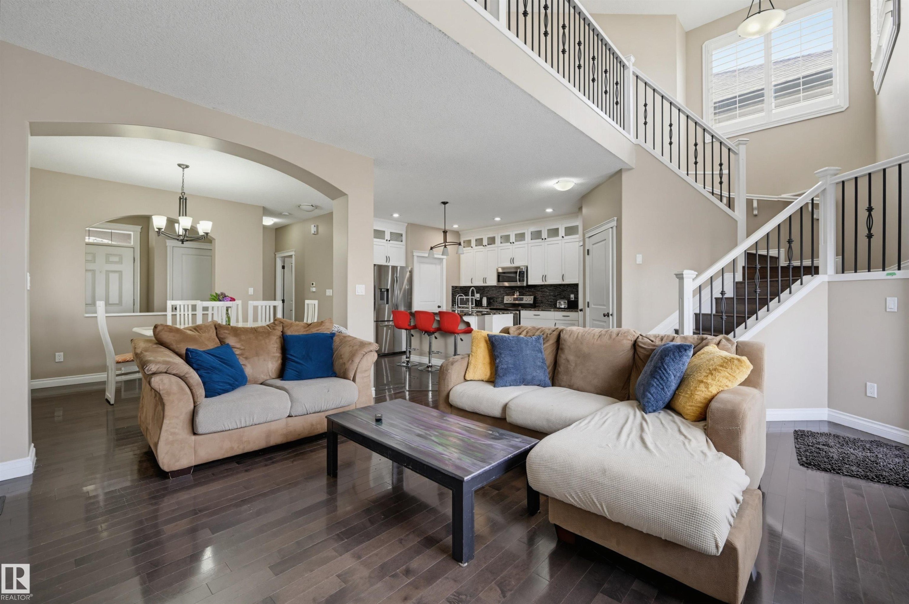 Open-concept interior featuring wood-finish flooring, a two-story ceiling, and a staircase with wrought iron balusters - 21928 97 Avenue Nw, Edmonton, AB - Indoor Photo Showing Living Room