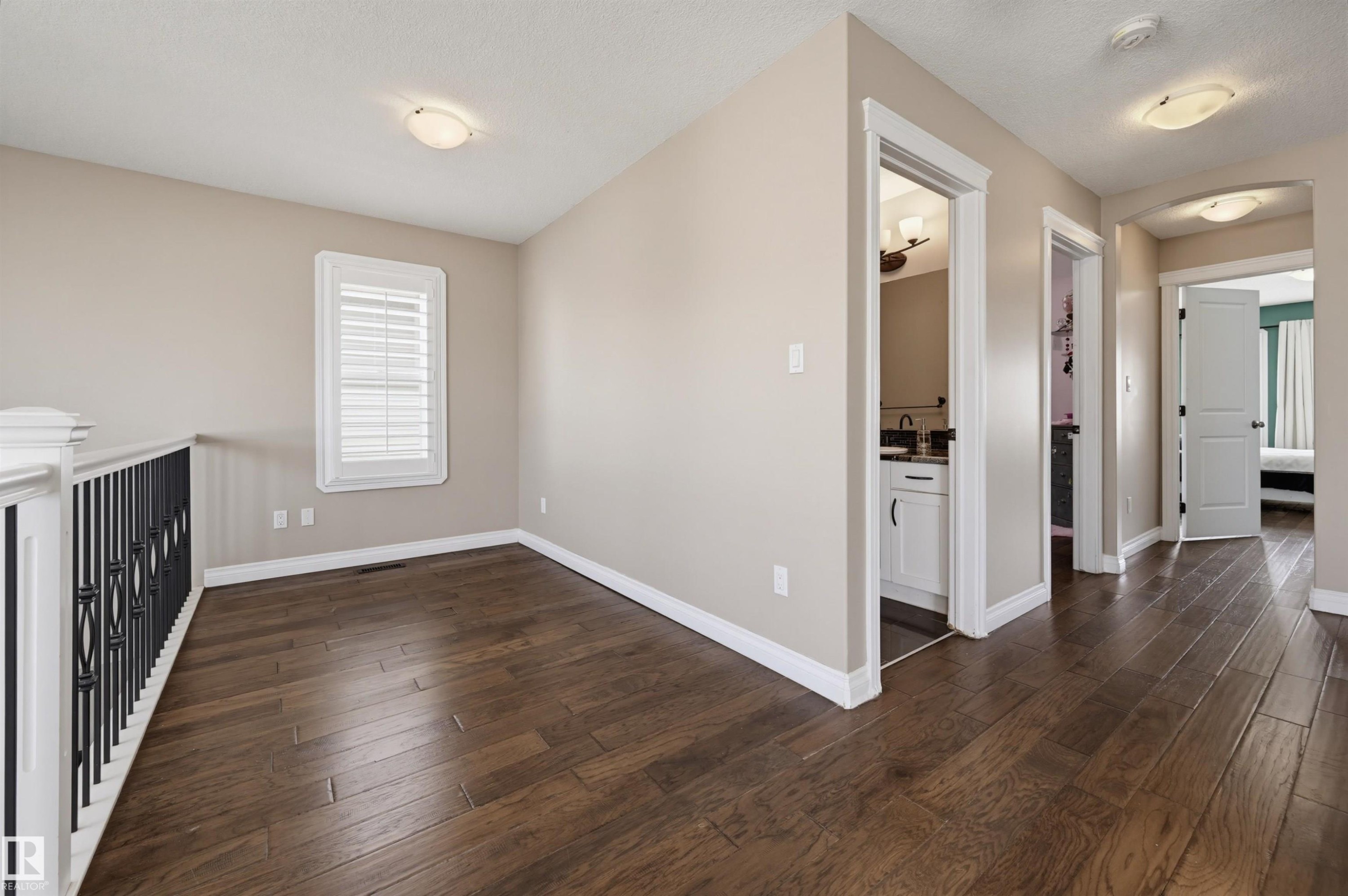 Upper-level hallway featuring wood-finish flooring, neutral wall tones, white baseboards, and a white window with louvered shutters - 21928 97 Avenue Nw, Edmonton, AB - Indoor Photo Showing Other Room