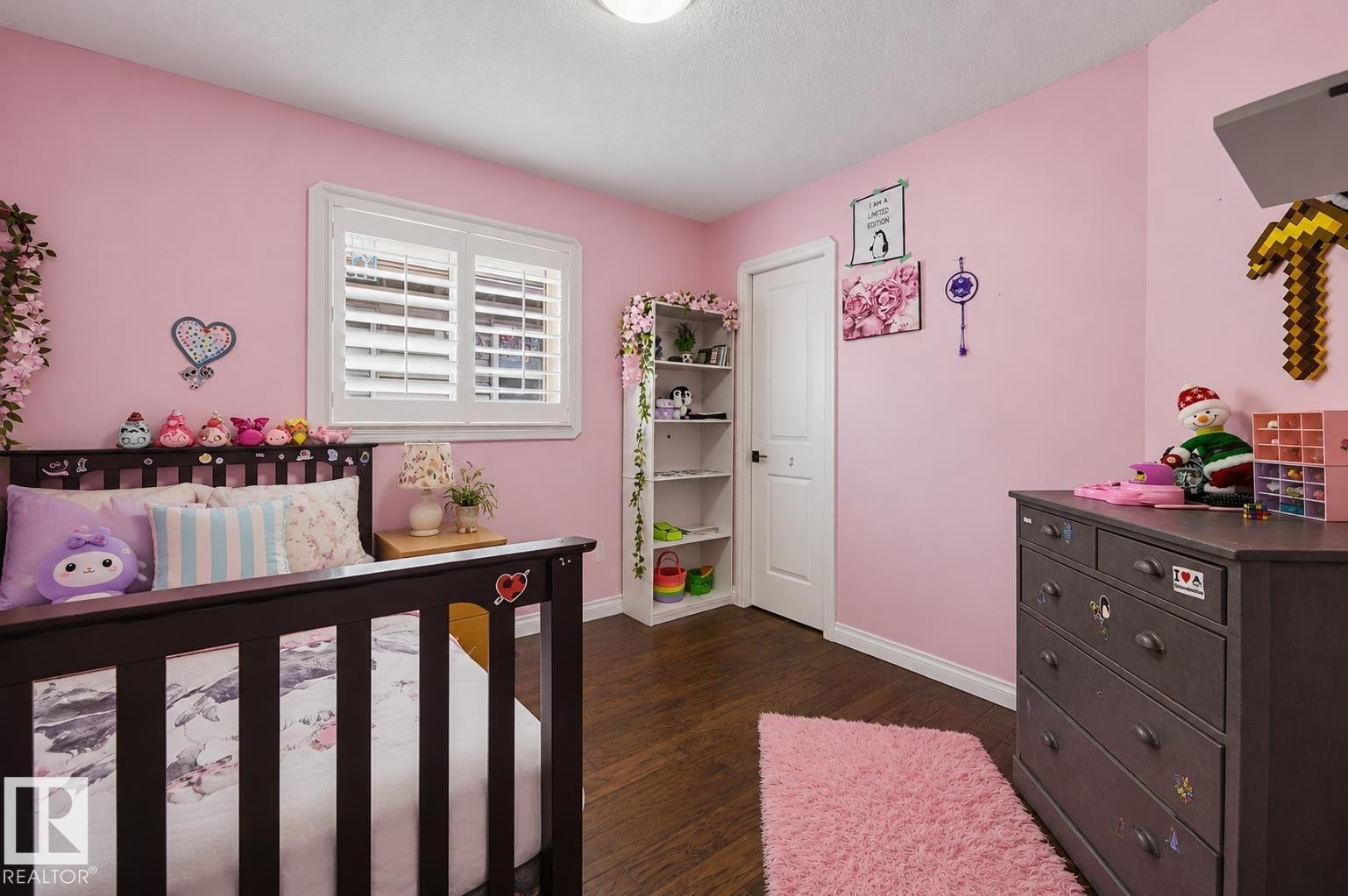 Bedroom featuring wood-finish flooring, a window with white louvered shutters, a white door, and a built-in shelving unit - 21928 97 Avenue Nw, Edmonton, AB - Indoor Photo Showing Bedroom