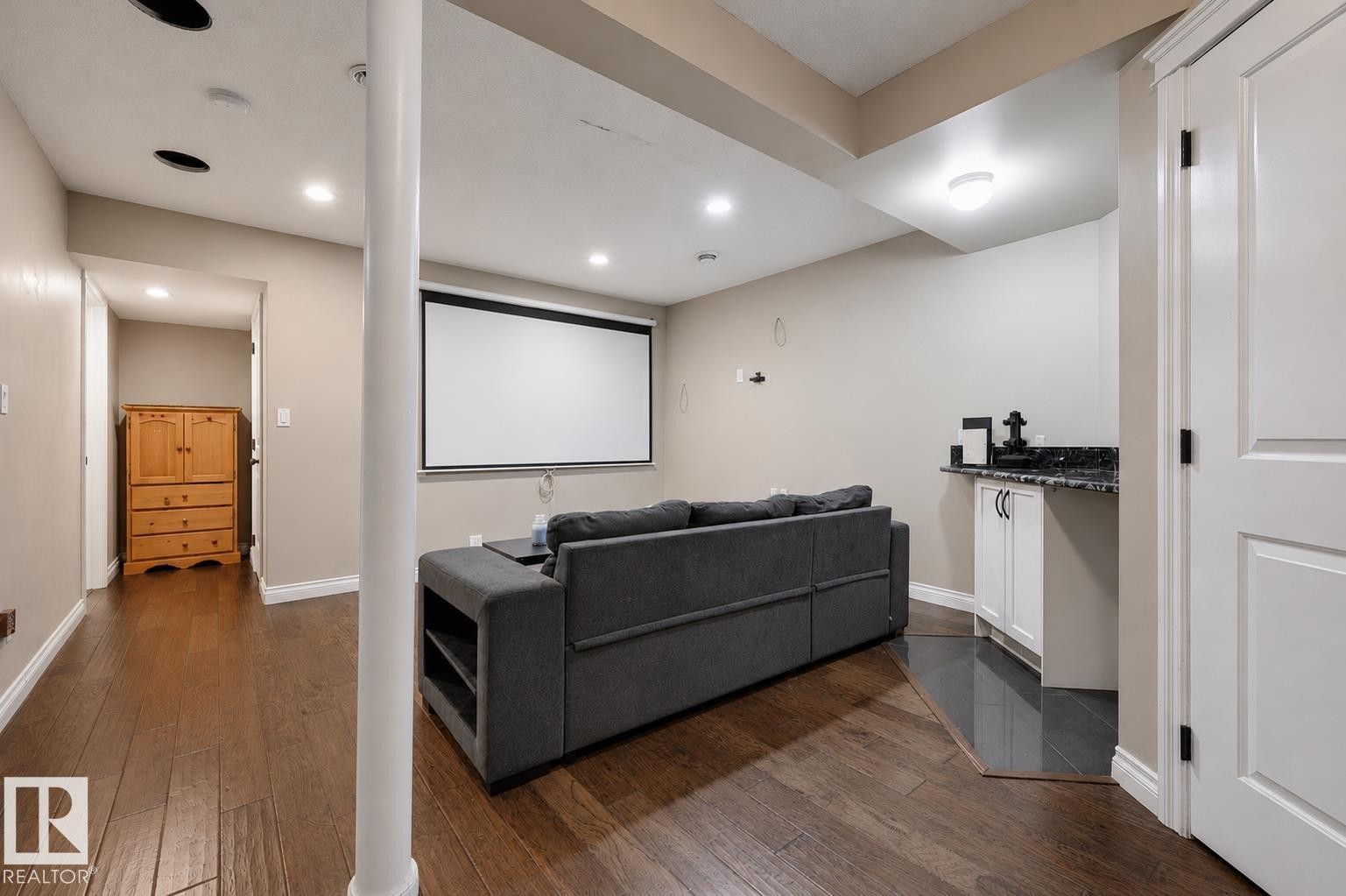 Recreation area featuring a projector screen, recessed lighting, wood-finish flooring, and a built-in wet bar with a dark countertop and white cabinetry - 21928 97 Avenue Nw, Edmonton, AB - Indoor