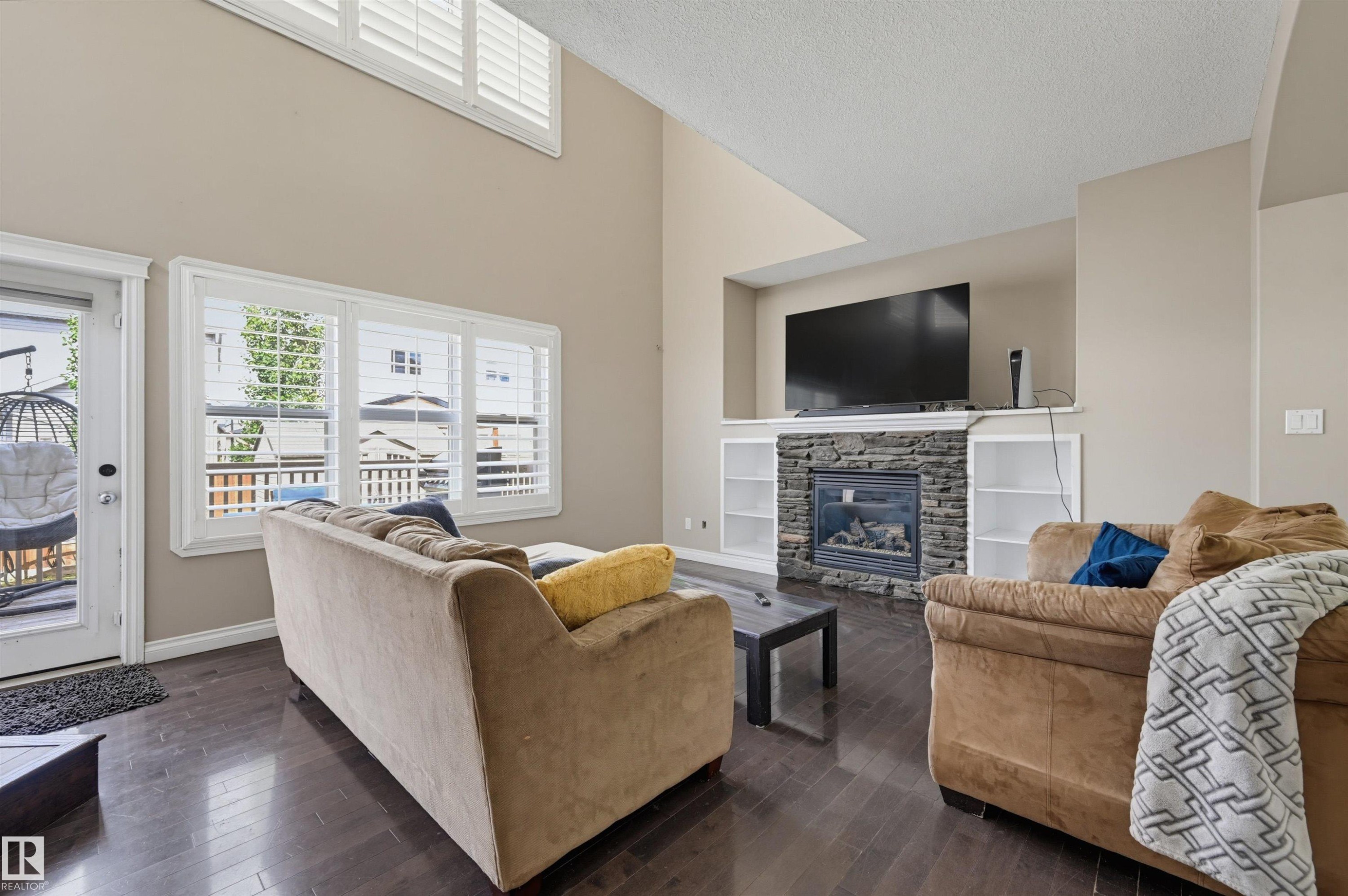 Living room with vaulted ceiling, wood-finish flooring, and a stone-clad fireplace with built-in shelving - 21928 97 Avenue Nw, Edmonton, AB - Indoor Photo Showing Living Room With Fireplace