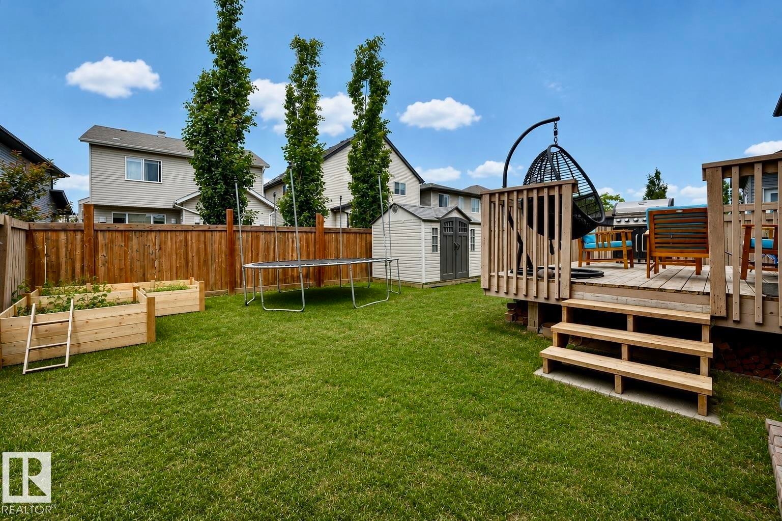 Expansive backyard featuring a wood deck with railings, a manicured lawn, a privacy fence, and two raised garden beds - 21928 97 Avenue Nw, Edmonton, AB - Outdoor With Deck Patio Veranda