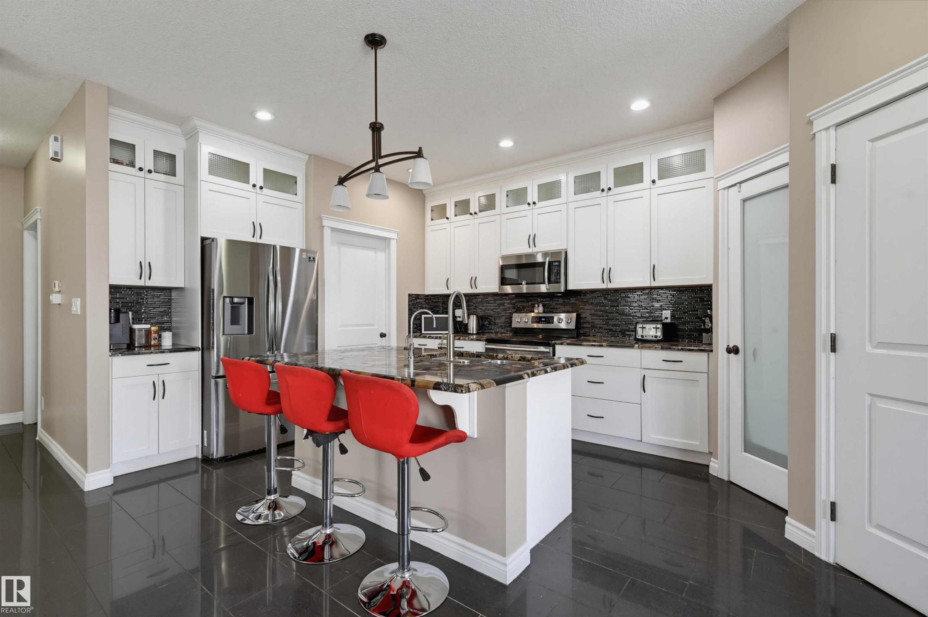 Kitchen featuring a large central island with seating, white cabinetry, dark stone countertops, and stainless steel appliances - 21928 97 Avenue Nw, Edmonton, AB - Indoor Photo Showing Kitchen With Upgraded Kitchen