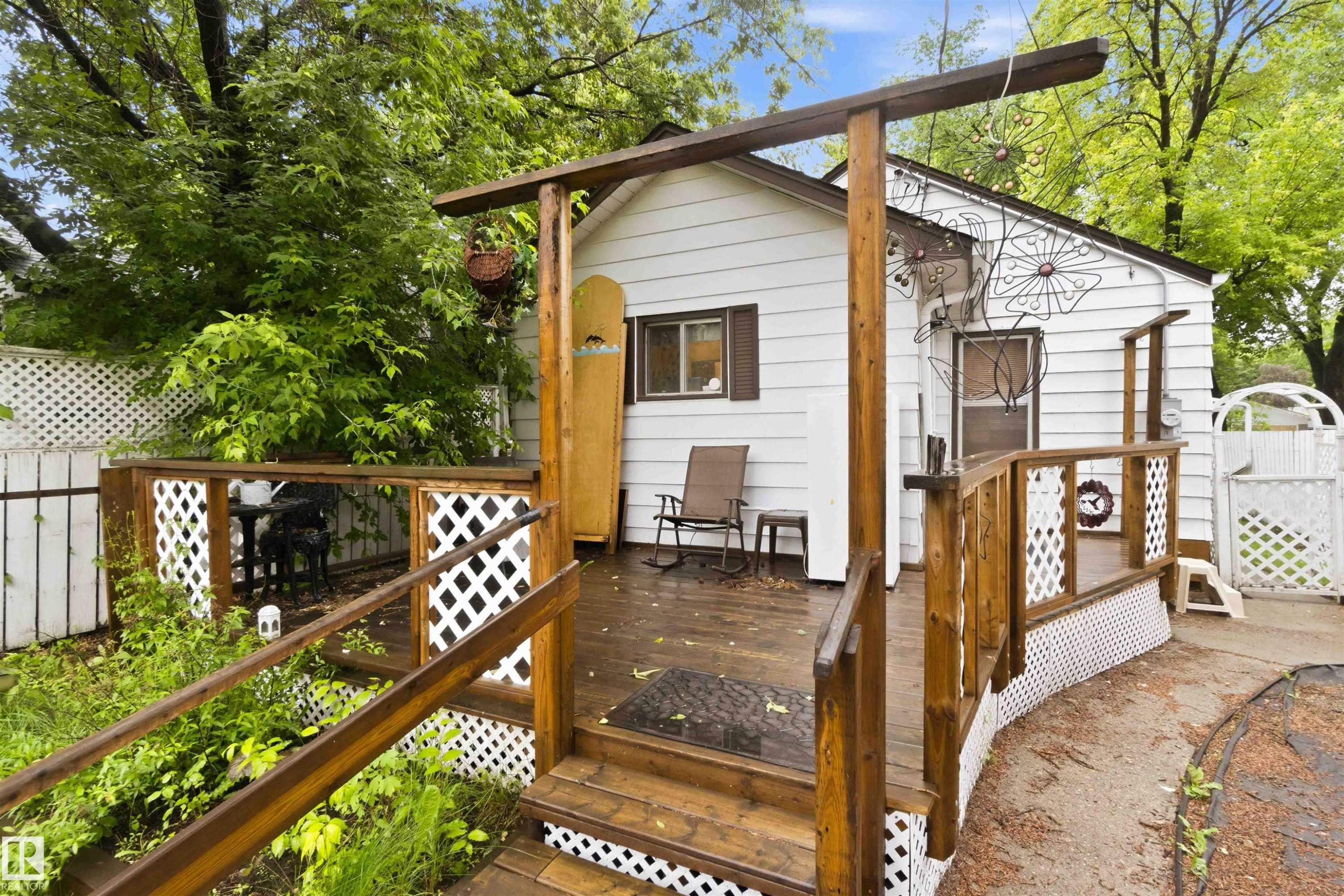 Exterior white siding residence featuring a wooden deck with railing, lattice accents, a ramp, and steps - 12016 61 Street, Edmonton, AB