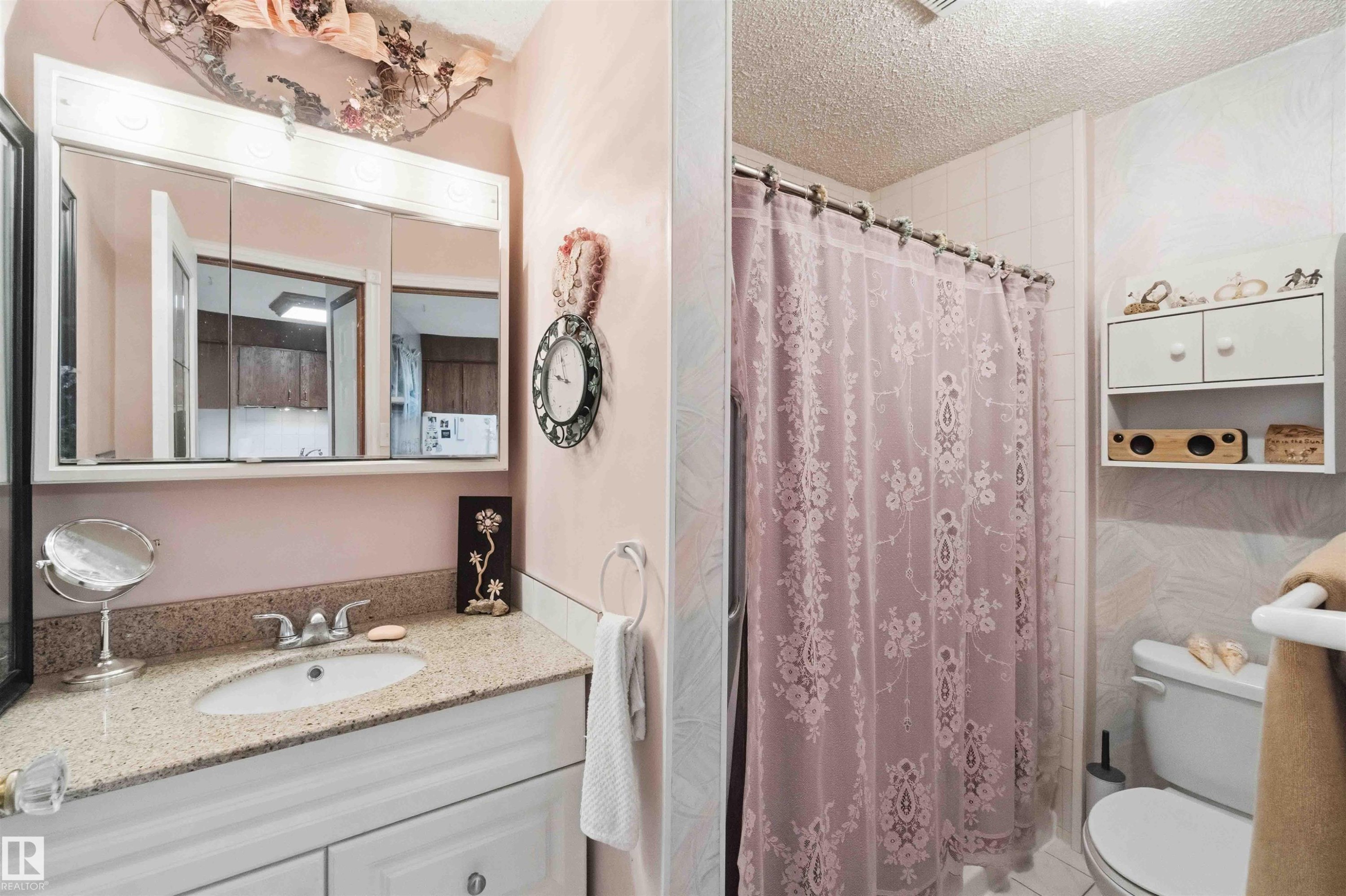Bathroom featuring a white vanity with paneling, a light-toned speckled countertop, and a built-in medicine cabinet with mirrored doors - 12016 61 Street, Edmonton, AB