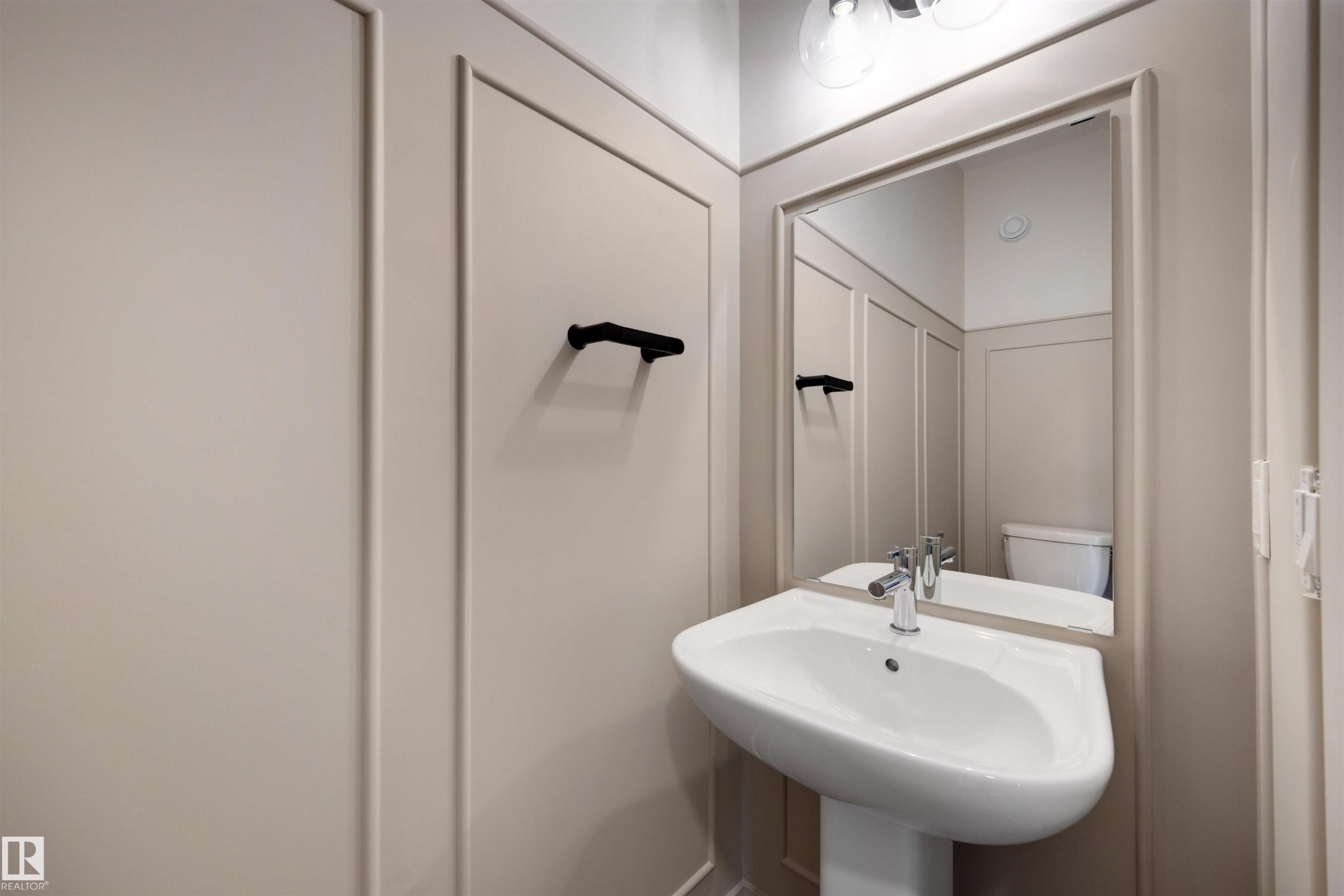 Powder room featuring wainscoting, a pedestal sink with chrome faucet, and an overhead vanity light fixture - 24 Grayson Green, Stony Plain, AB