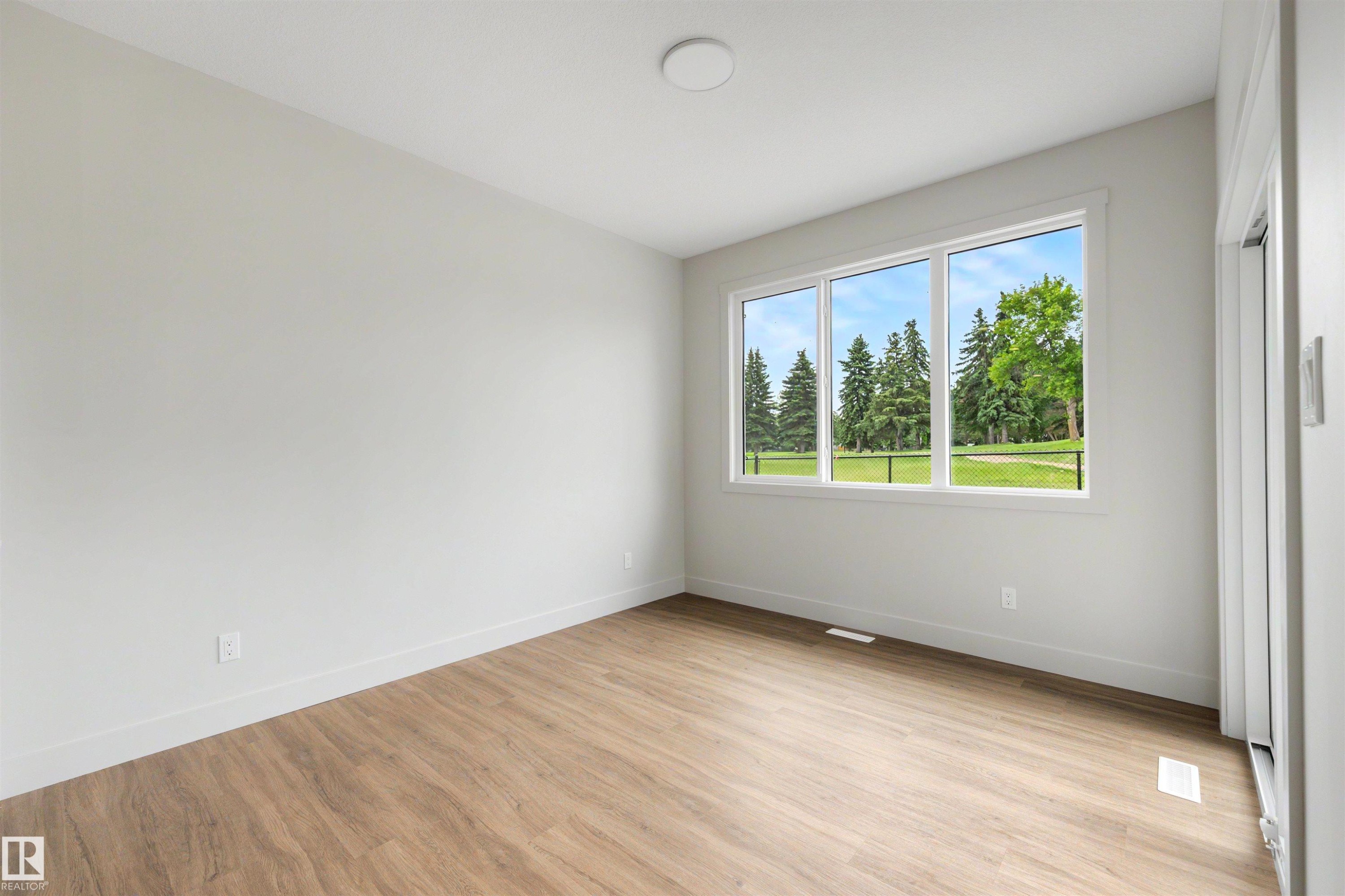 Bright room featuring wood-finish flooring, white baseboards, and a large multi-pane window with a verdant outdoor landscape - 24 Grayson Green, Stony Plain, AB
