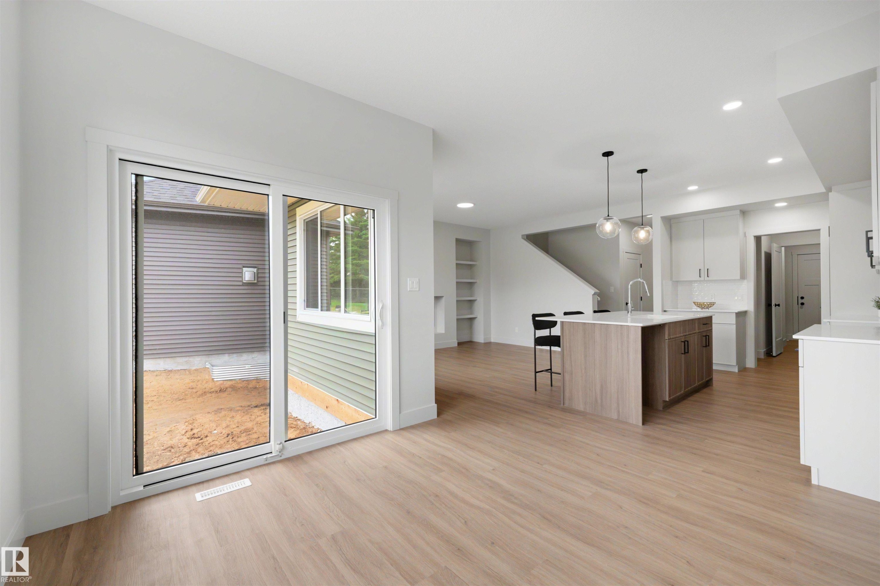 Open concept living space featuring wood-finish flooring, a kitchen island with seating, pendant lighting, and recessed ceiling lights - 24 Grayson Green, Stony Plain, AB