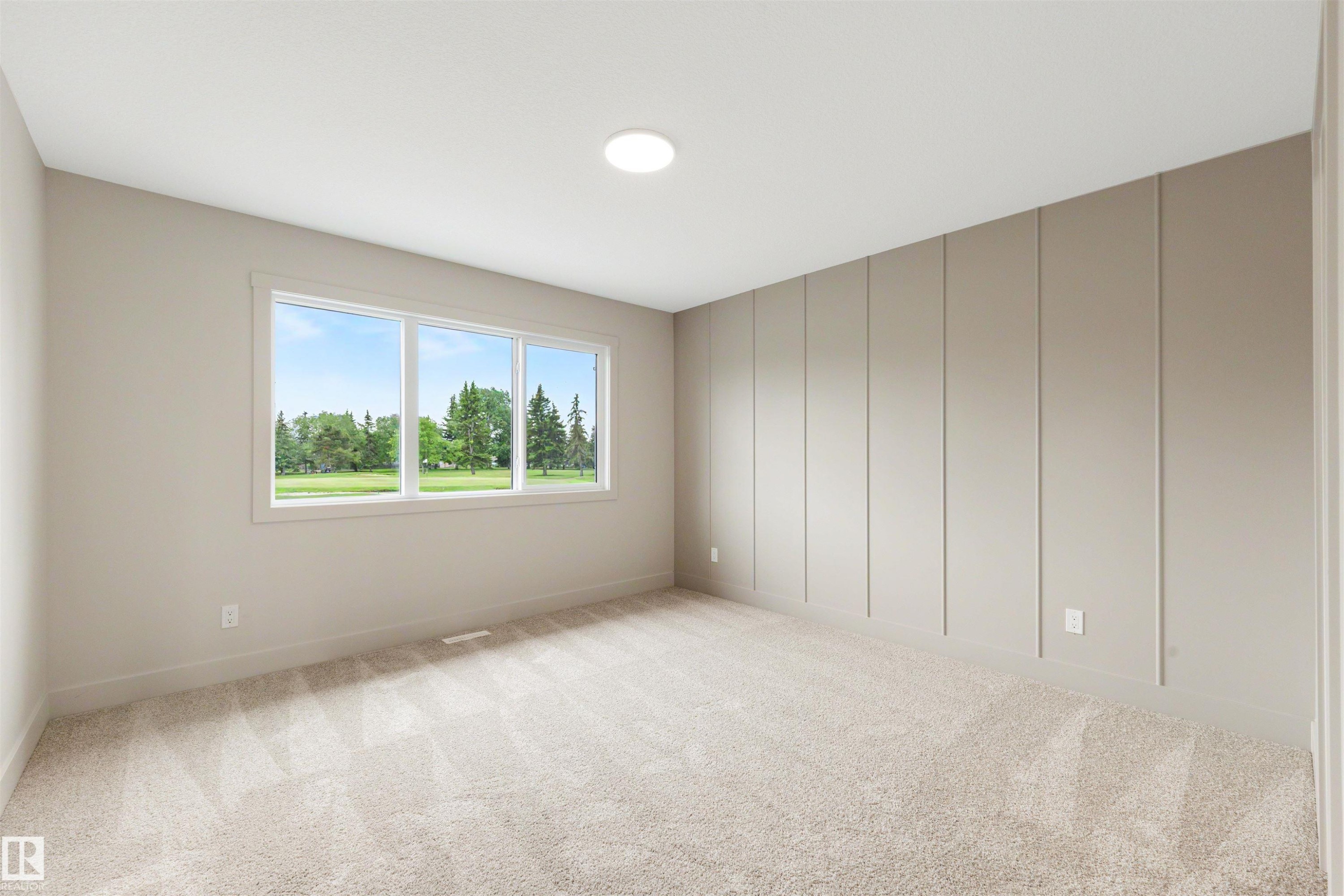 Expansive room featuring a large three-panel window, light-toned carpet flooring, a decorative panel accent wall, and recessed ceiling lighting - 24 Grayson Green, Stony Plain, AB