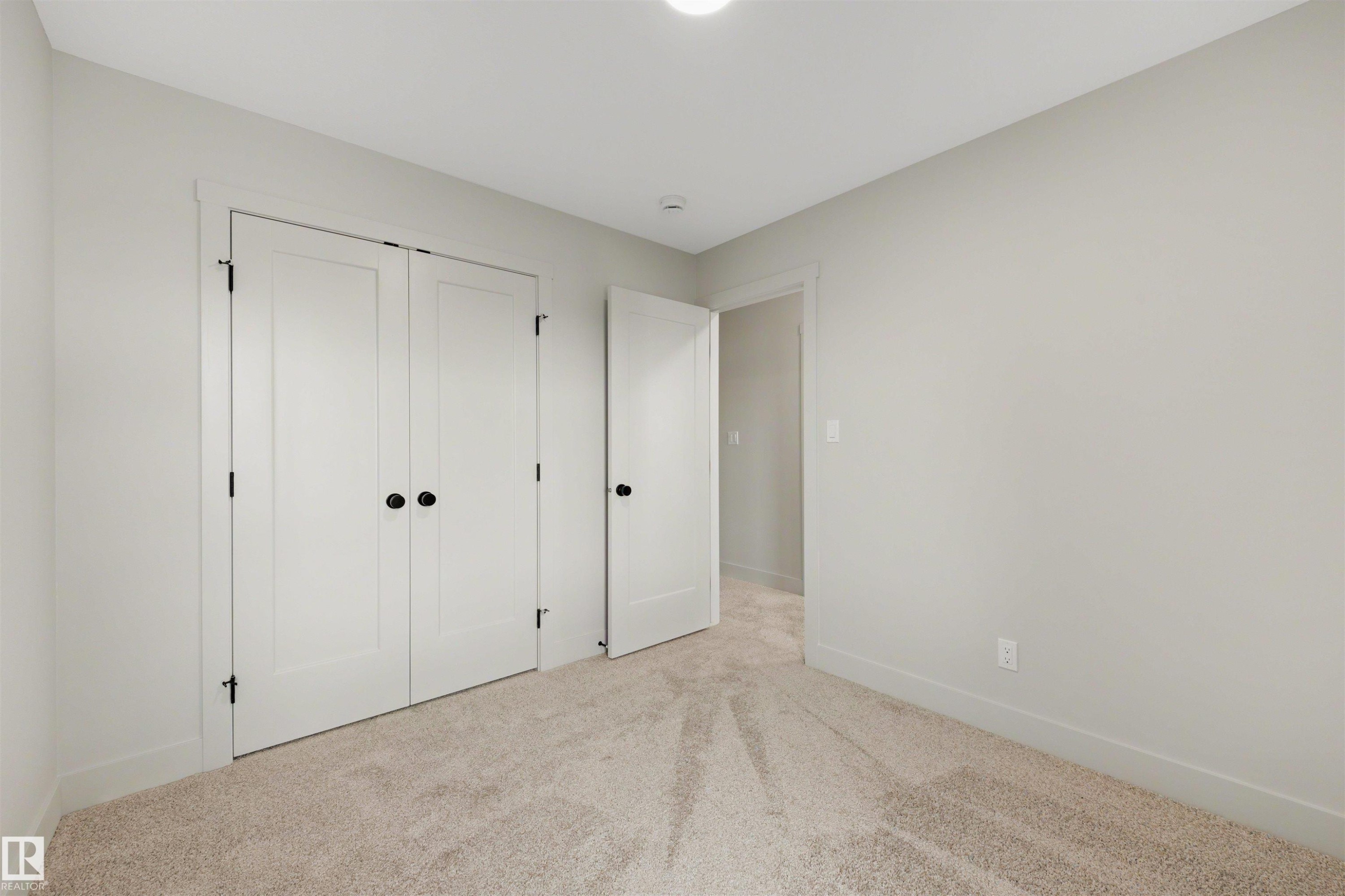 Neutral-toned room featuring a soft carpet, white baseboards, and a pair of white double doors with matte black hardware - 24 Grayson Green, Stony Plain, AB
