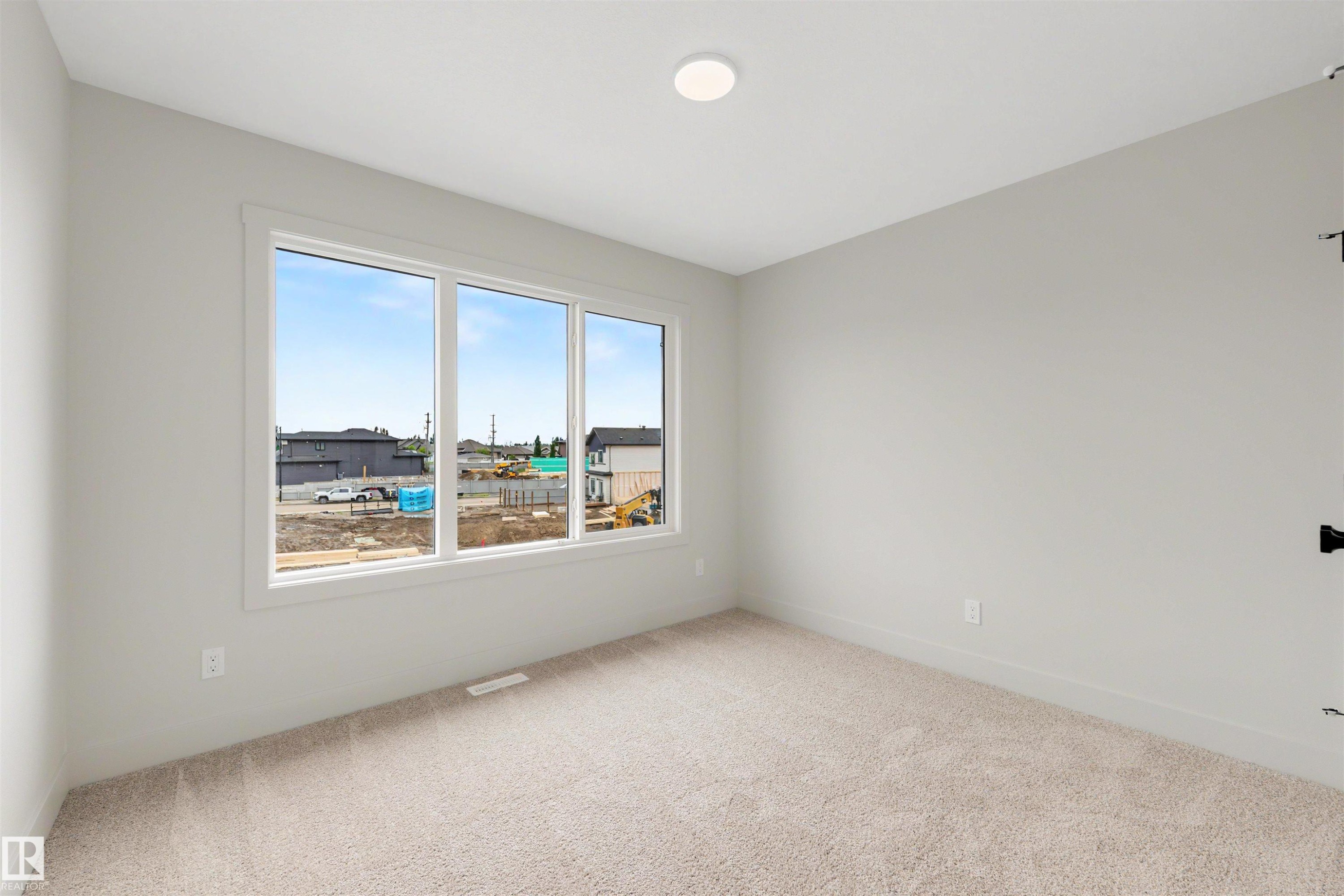 Bright room featuring a triple window unit, plush carpeting, light gray walls, white trim, and a flush-mount ceiling light fixture - 24 Grayson Green, Stony Plain, AB