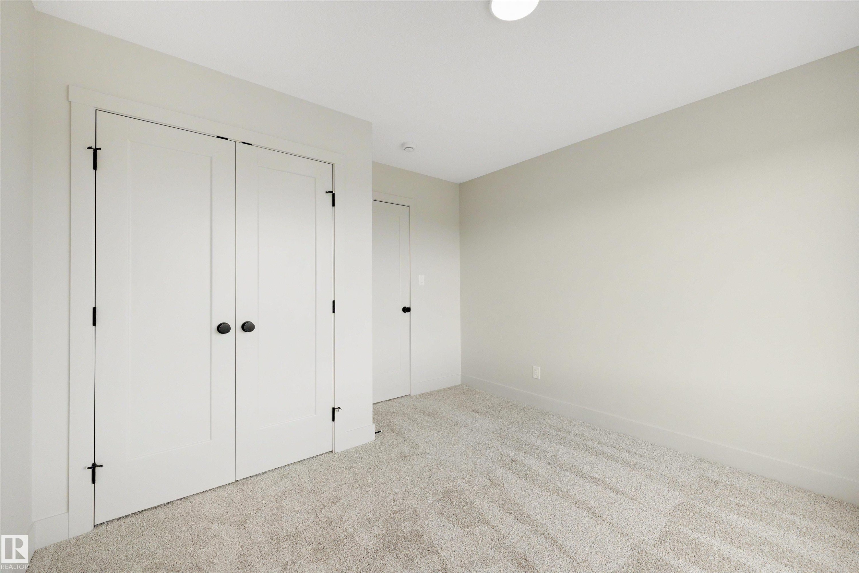 Neutral-toned room featuring a light-colored carpet, white walls, and a white ceiling with a flush-mount light fixture - 24 Grayson Green, Stony Plain, AB