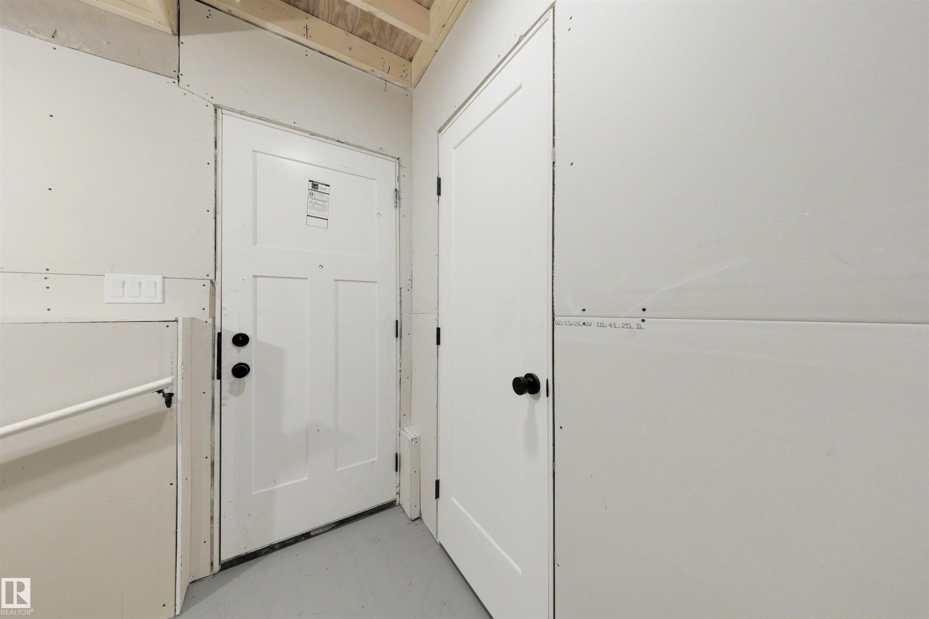 Interior space featuring a white paneled door with matte black hardware, white walls, and exposed wood ceiling framing - 24 Grayson Green, Stony Plain, AB