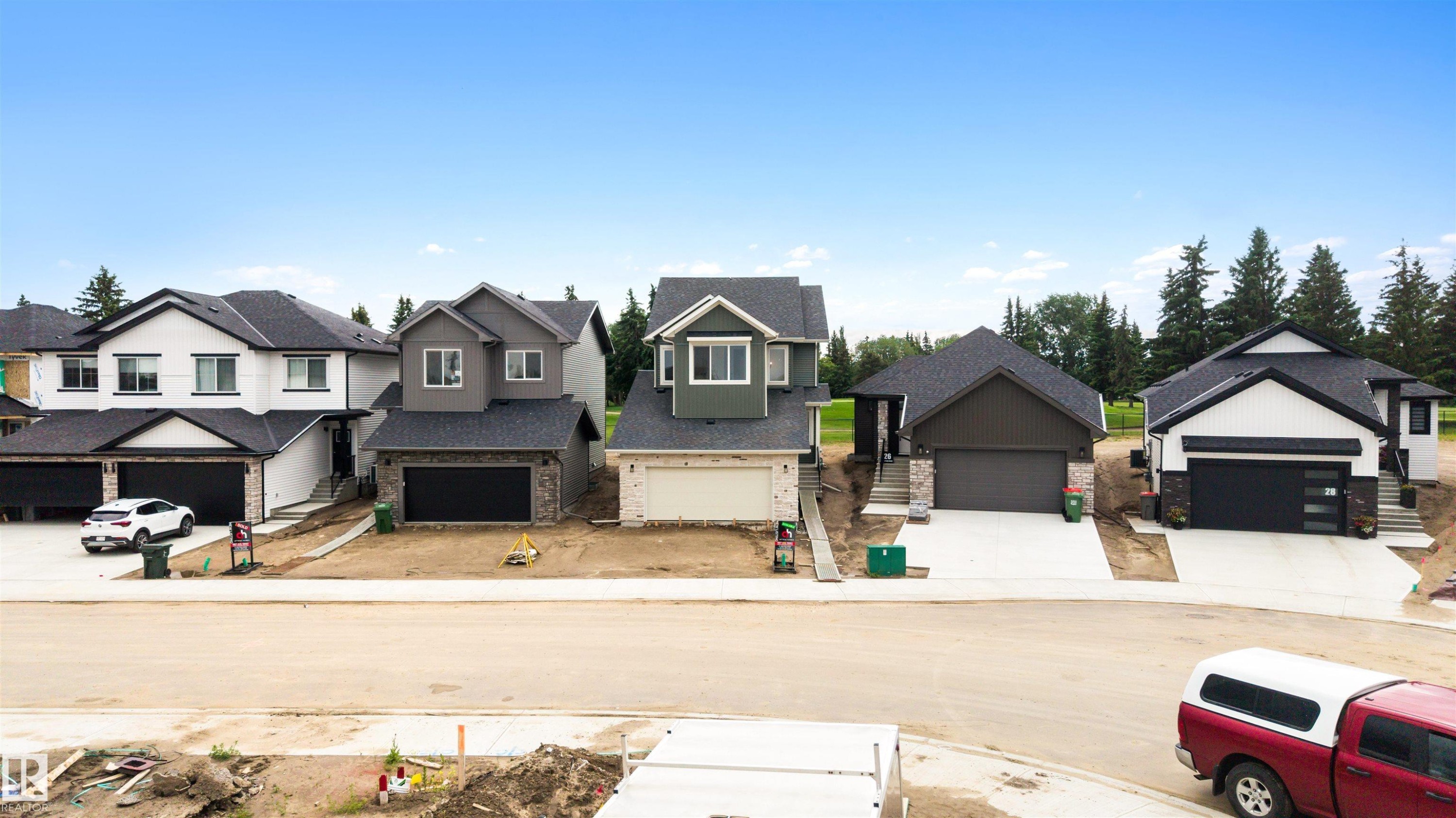 Modern residences featuring dark roofing, attached garages, and a mix of exterior siding and stone accents - 24 Grayson Green, Stony Plain, AB