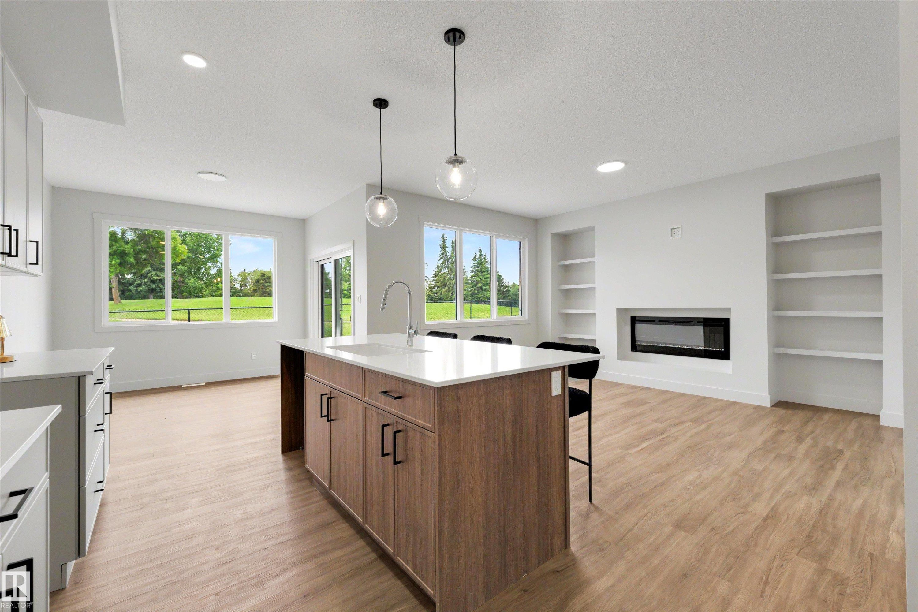 Open-concept living area featuring a kitchen island with built-in cabinetry, quartz countertops, and a stainless steel sink - 24 Grayson Green, Stony Plain, AB