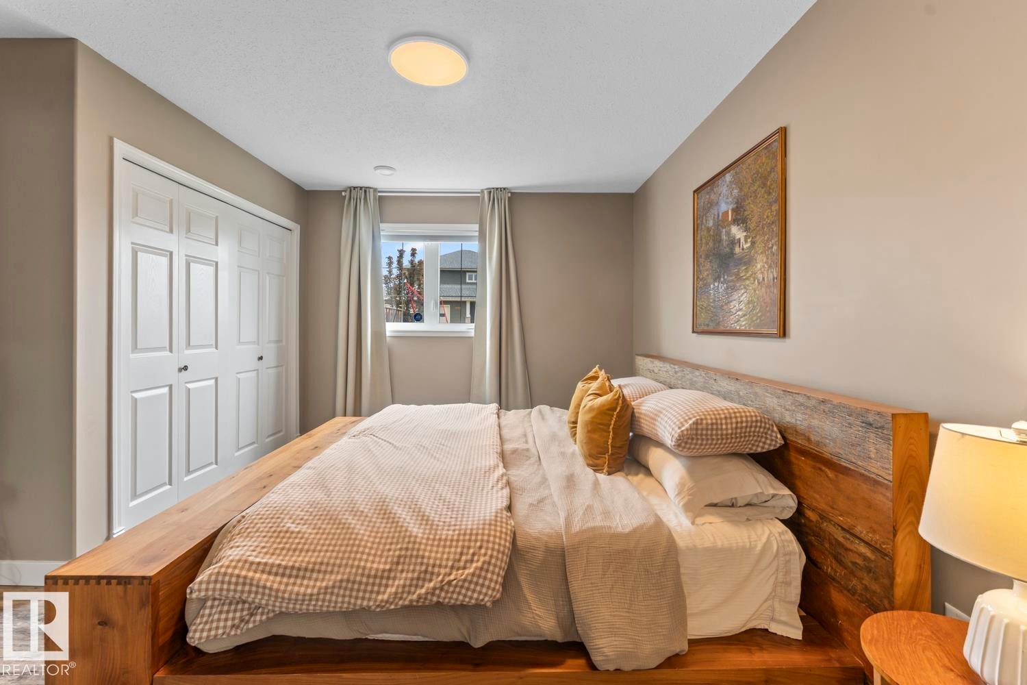 Bedroom featuring a large window with soft drapes, closet with bifold panel doors, and neutral wall tones - 2602 Delta Road, Cold Lake, AB