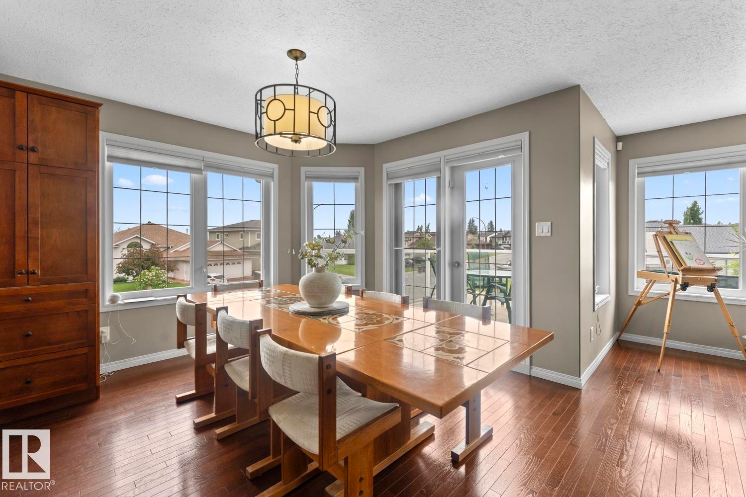 Dining area featuring wood-finish flooring, a contemporary ceiling fixture, built-in cabinetry, and multiple large windows with grid patterns - 2602 Delta Road, Cold Lake, AB