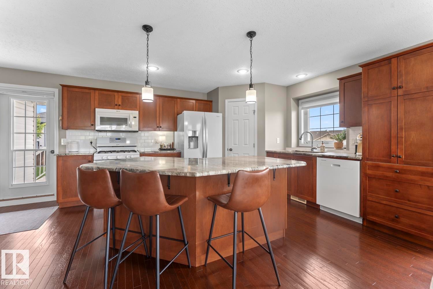 Kitchen featuring a central island with countertop seating, wood-finish flooring, white subway tile backsplash, and a built-in pantry cabinet - 2602 Delta Road, Cold Lake, AB