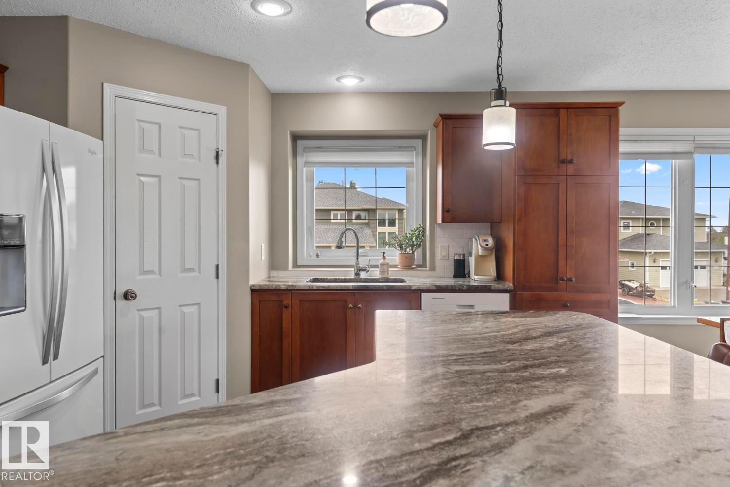 Kitchen featuring a large island with a patterned countertop, wood cabinetry, recessed lighting, a pendant light fixture, and a kitchen sink with a gooseneck faucet - 2602 Delta Road, Cold Lake, AB