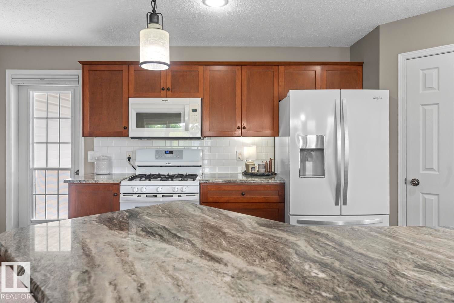 Kitchen featuring an expansive stone-finish countertop, wood cabinetry, white subway tile backsplash, and a white appliance suite - 2602 Delta Road, Cold Lake, AB