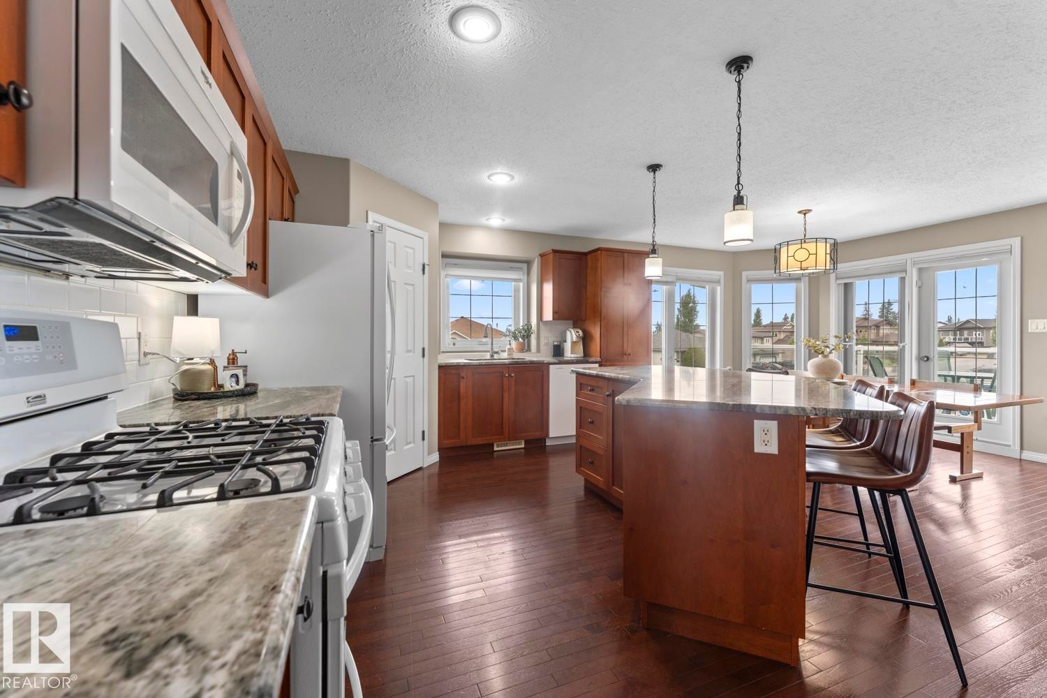 Open-concept kitchen featuring wood-finish flooring, a central island with countertop seating, recessed lighting, pendant lighting, and multiple window-paned doors - 2602 Delta Road, Cold Lake, AB