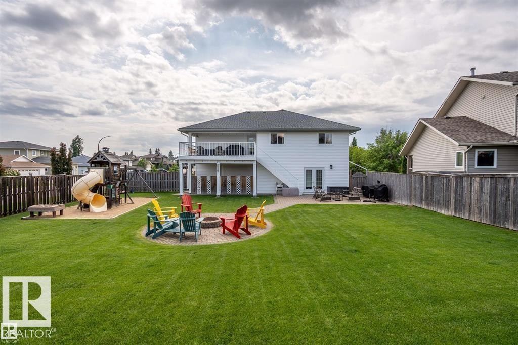 Expansive green lawn with a large paver patio, built-in fire pit, and a designated play area featuring a swing set and slide - 2602 Delta Road, Cold Lake, AB