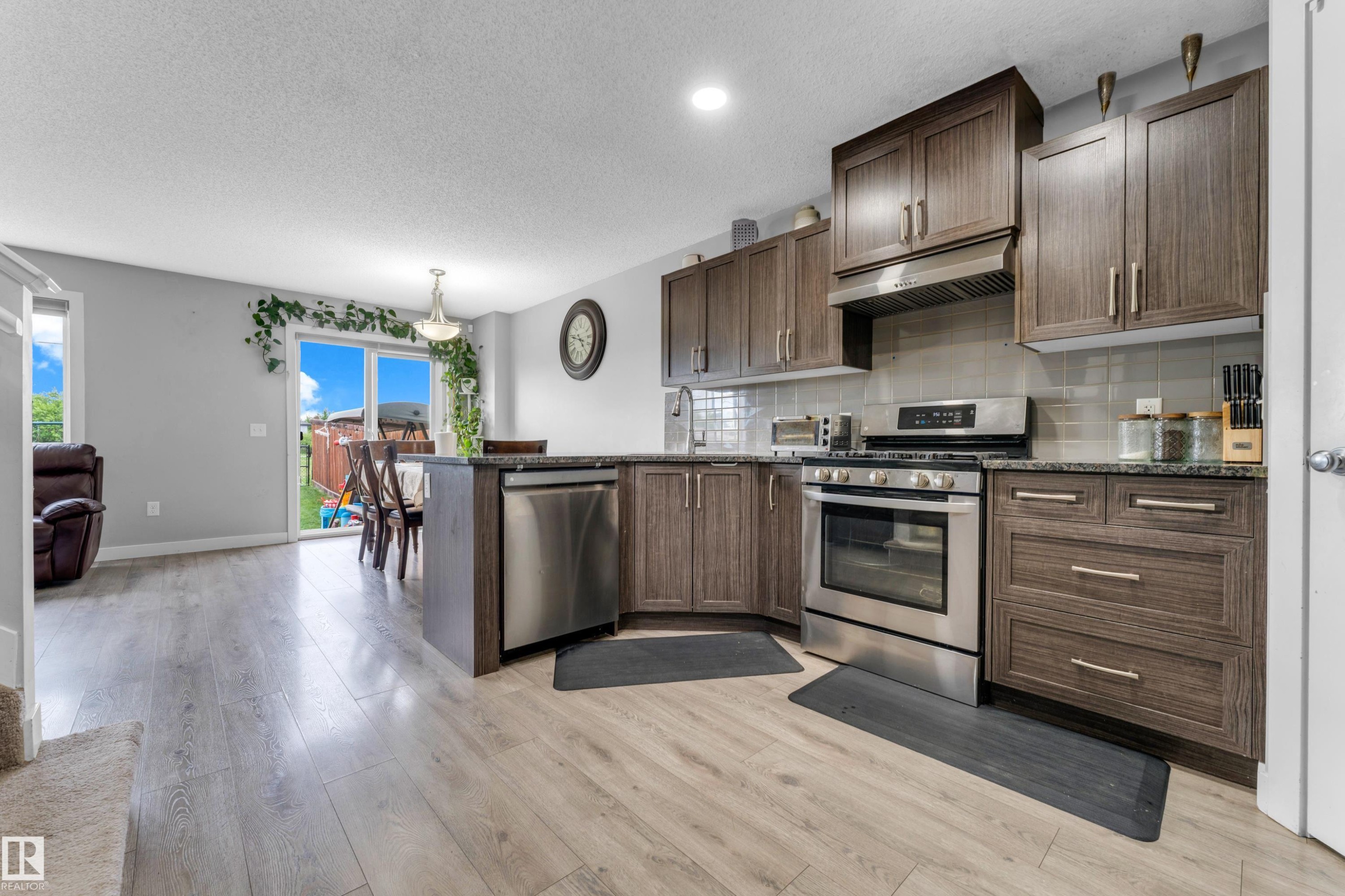 Open-concept kitchen featuring wood-finish cabinetry, stainless steel appliances, and light-toned wood-finish flooring - 1750 27 Street, Edmonton, AB