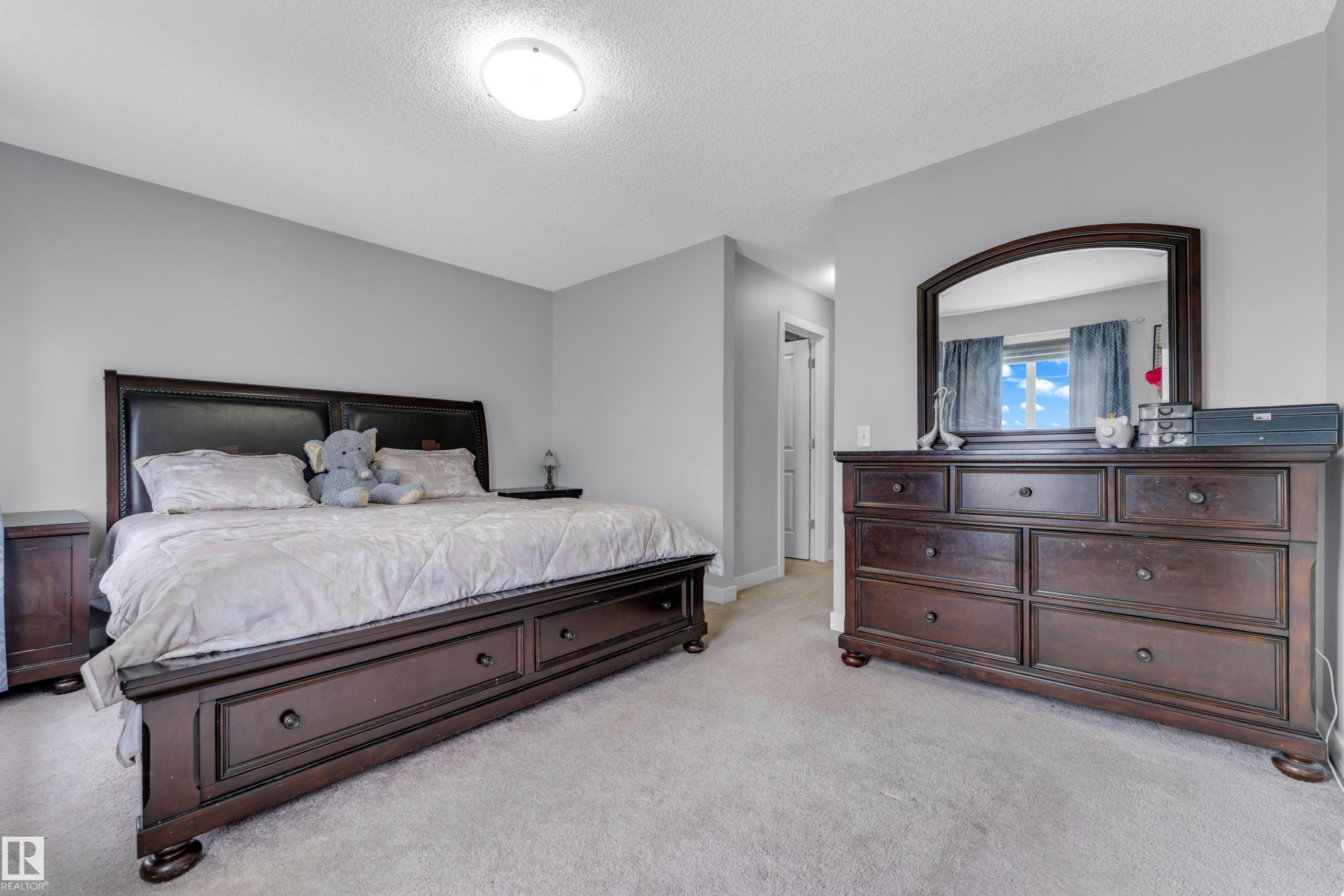 Carpeted bedroom with light gray walls, an overhead flush-mount light fixture, and a window with blue curtains - 1750 27 Street, Edmonton, AB