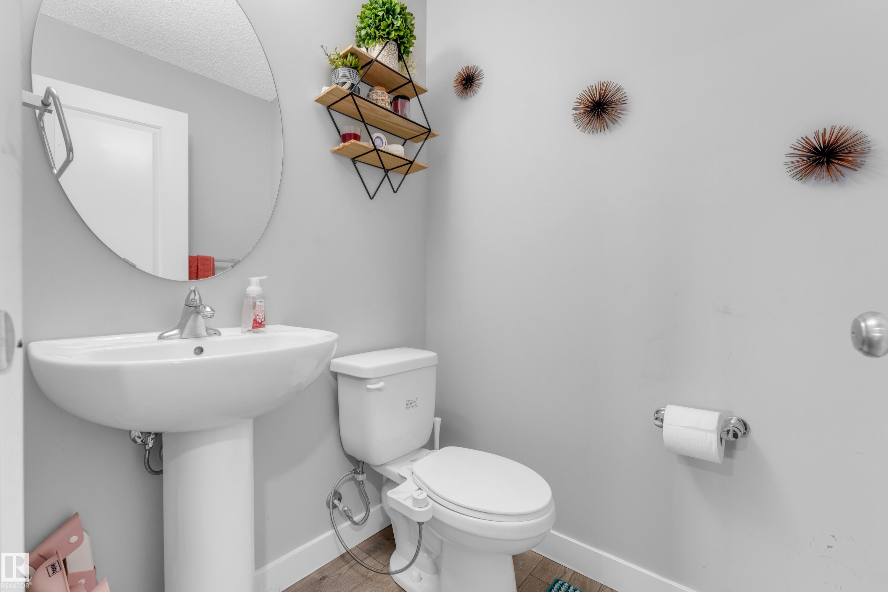 Pedestal sink with chrome faucet, oval mirror, and wood-finish flooring - 1750 27 Street, Edmonton, AB