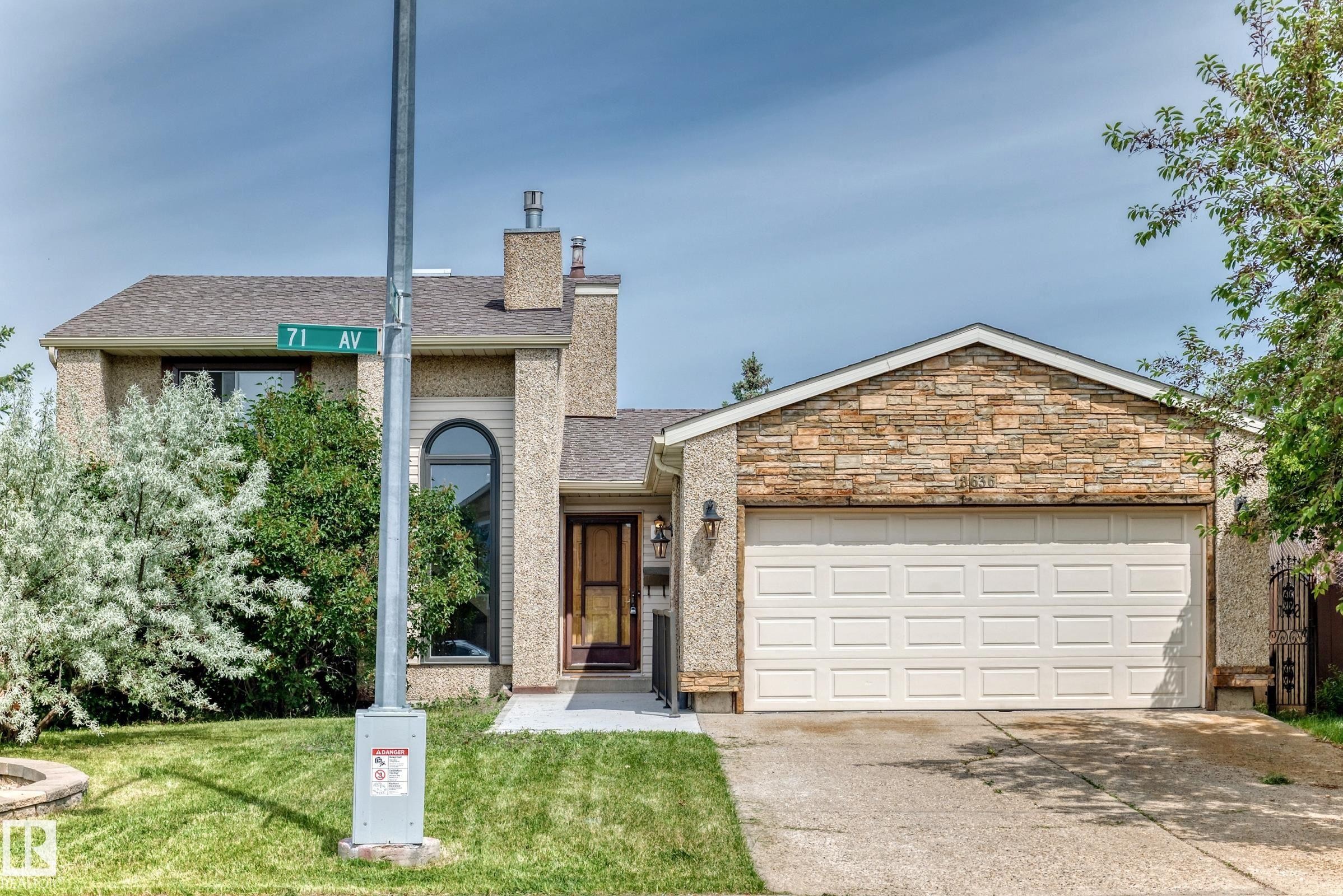 Residential exterior featuring a stone-clad garage gable, an arched window, a paneled garage door, a concrete driveway, and a shingle roof - 18636 71 Avenue, Edmonton, AB