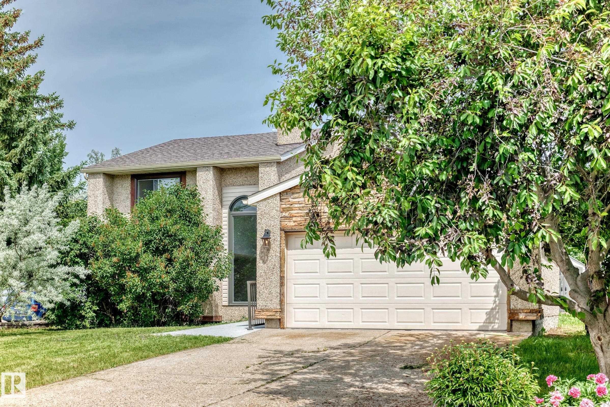 Stucco exterior residence with an attached garage, featuring a shingled roof, a tall arched window, and stone accents - 18636 71 Avenue, Edmonton, AB