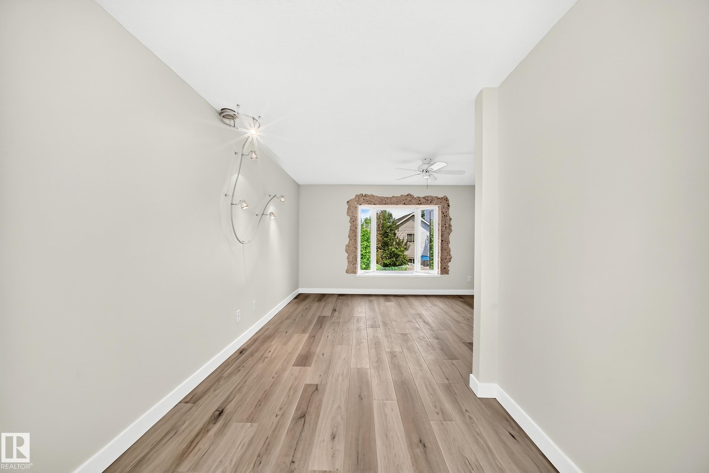 Expansive room featuring wide plank wood-finish flooring, a contemporary wall-mounted light fixture, crisp white baseboards, and a ceiling fan - 18636 71 Avenue, Edmonton, AB