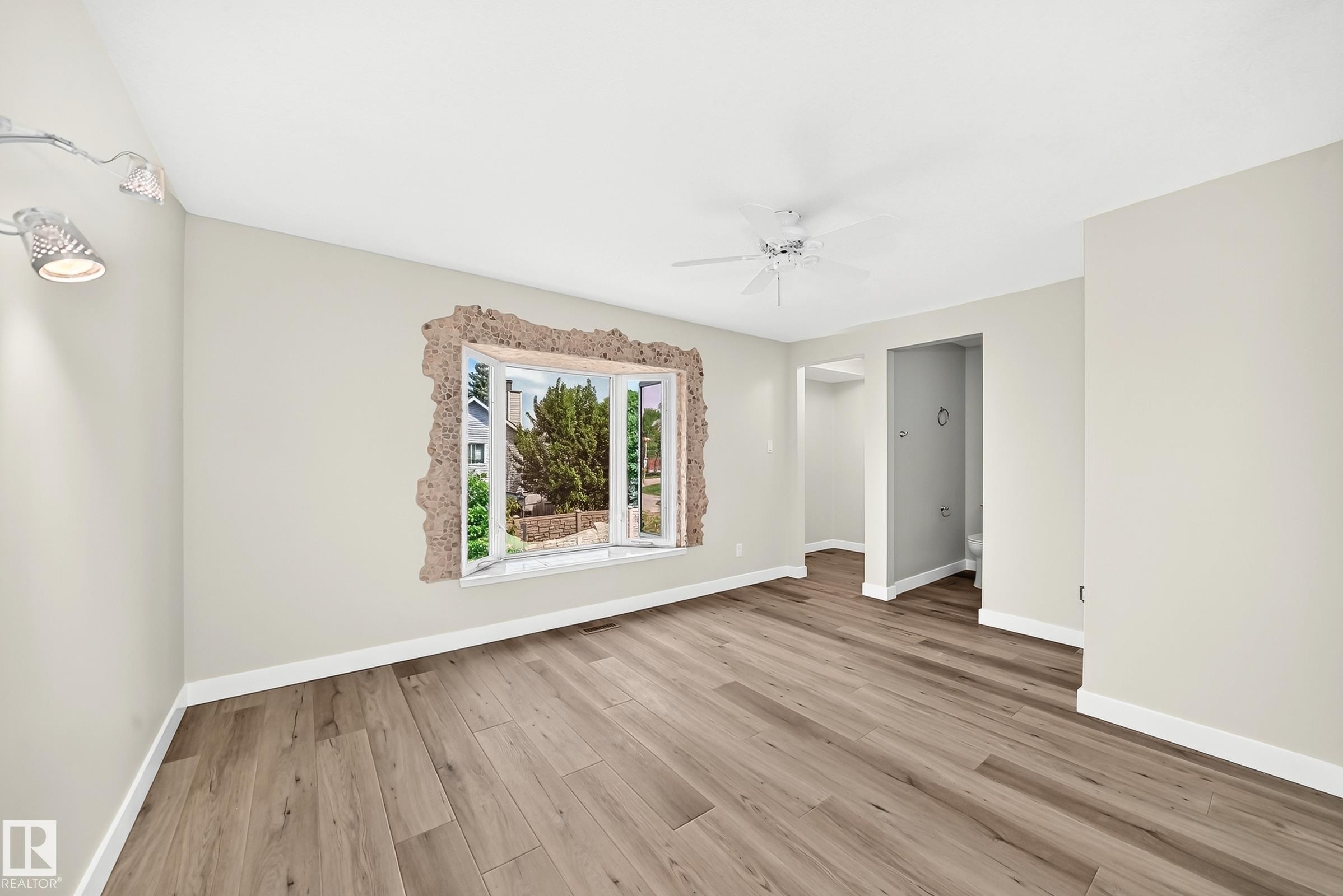 Spacious room featuring wood-finish flooring, light-toned walls, and a bay window - 18636 71 Avenue, Edmonton, AB