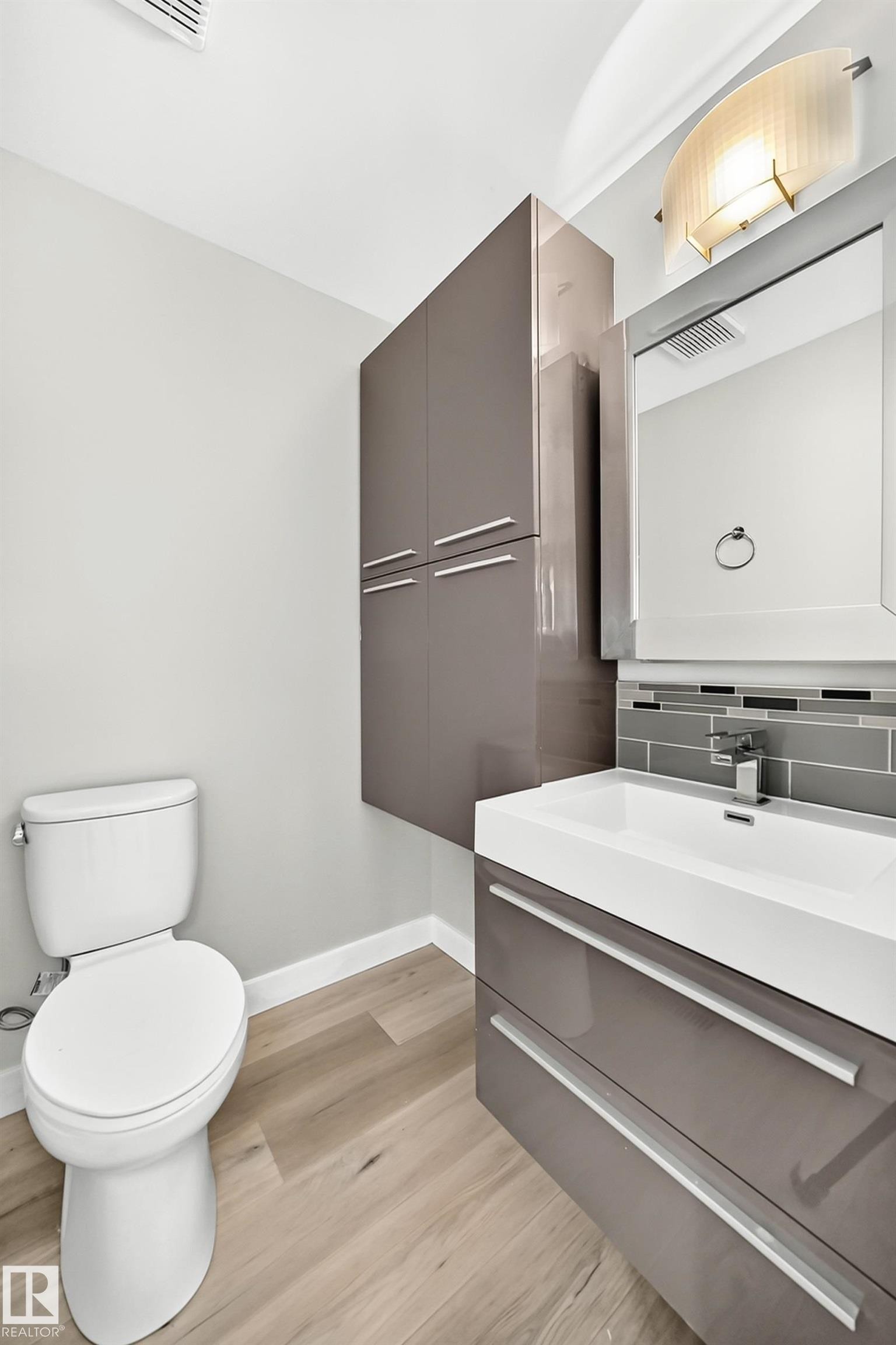 Contemporary bathroom featuring a floating vanity with integrated sink, sleek grey cabinetry, a modern wall-mounted light fixture, and wood-finish flooring - 18636 71 Avenue, Edmonton, AB