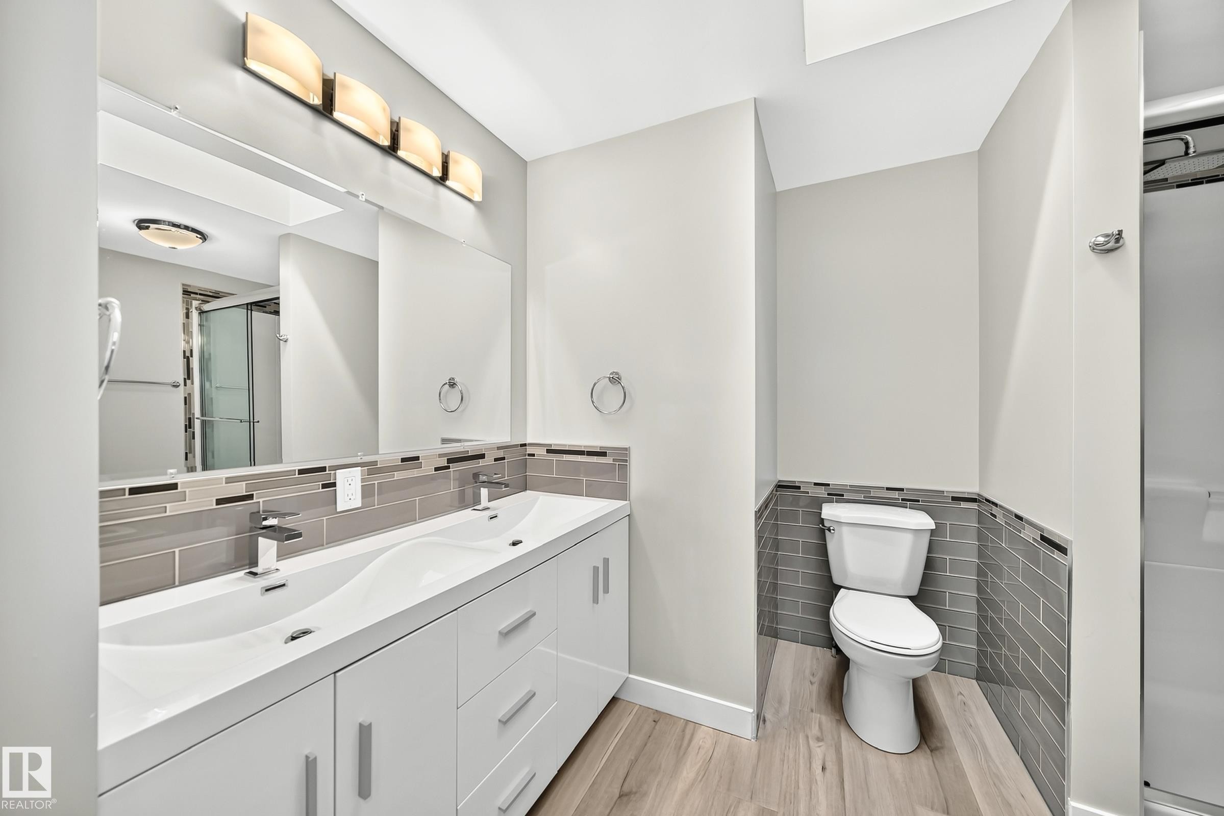 Modern bathroom featuring a dual-sink vanity with white cabinetry and chrome hardware, a large vanity mirror, and contemporary light fixture - 18636 71 Avenue, Edmonton, AB