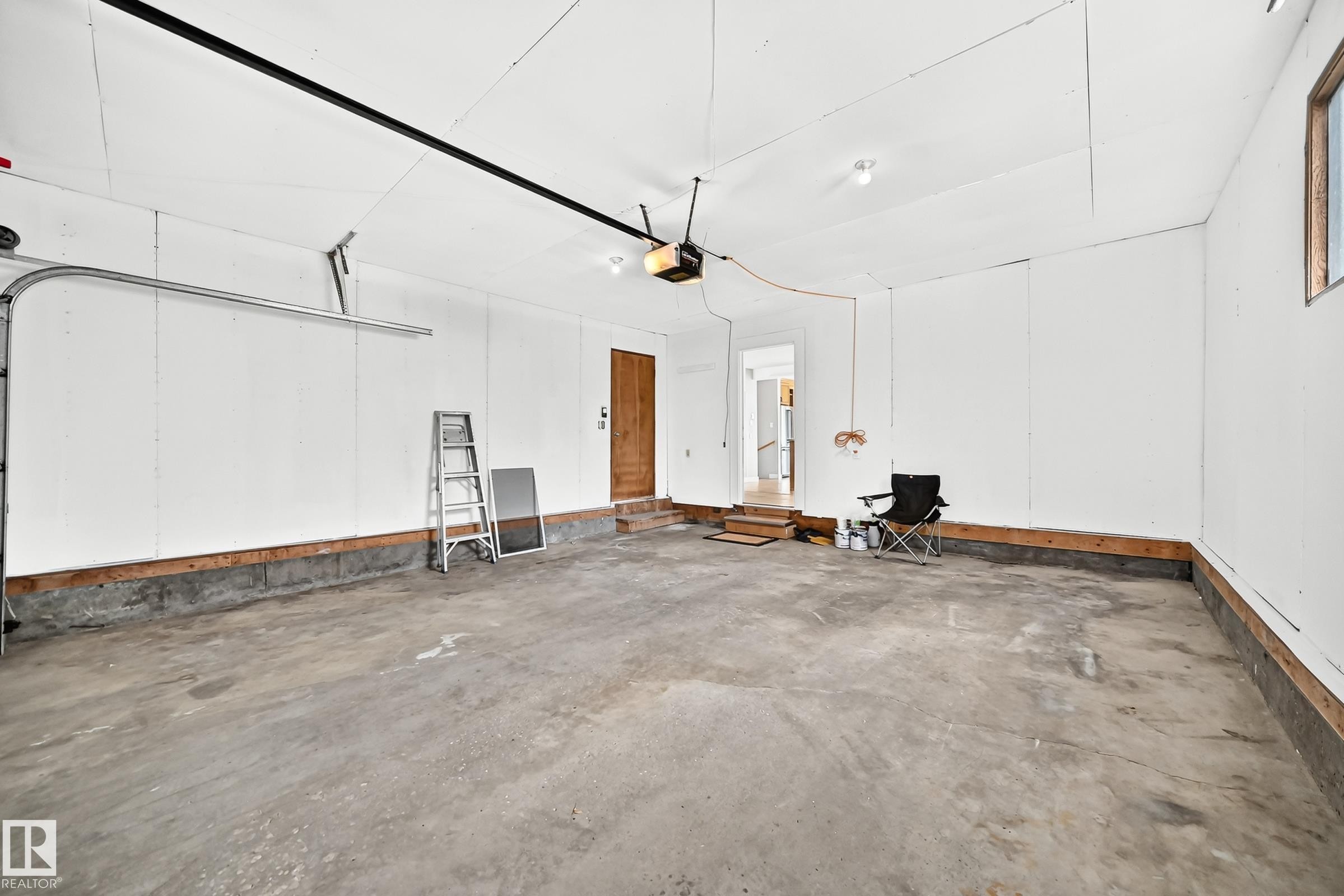 Spacious garage featuring a concrete floor, white walls, exposed wood framing at the base, and a single window for natural light - 18636 71 Avenue, Edmonton, AB