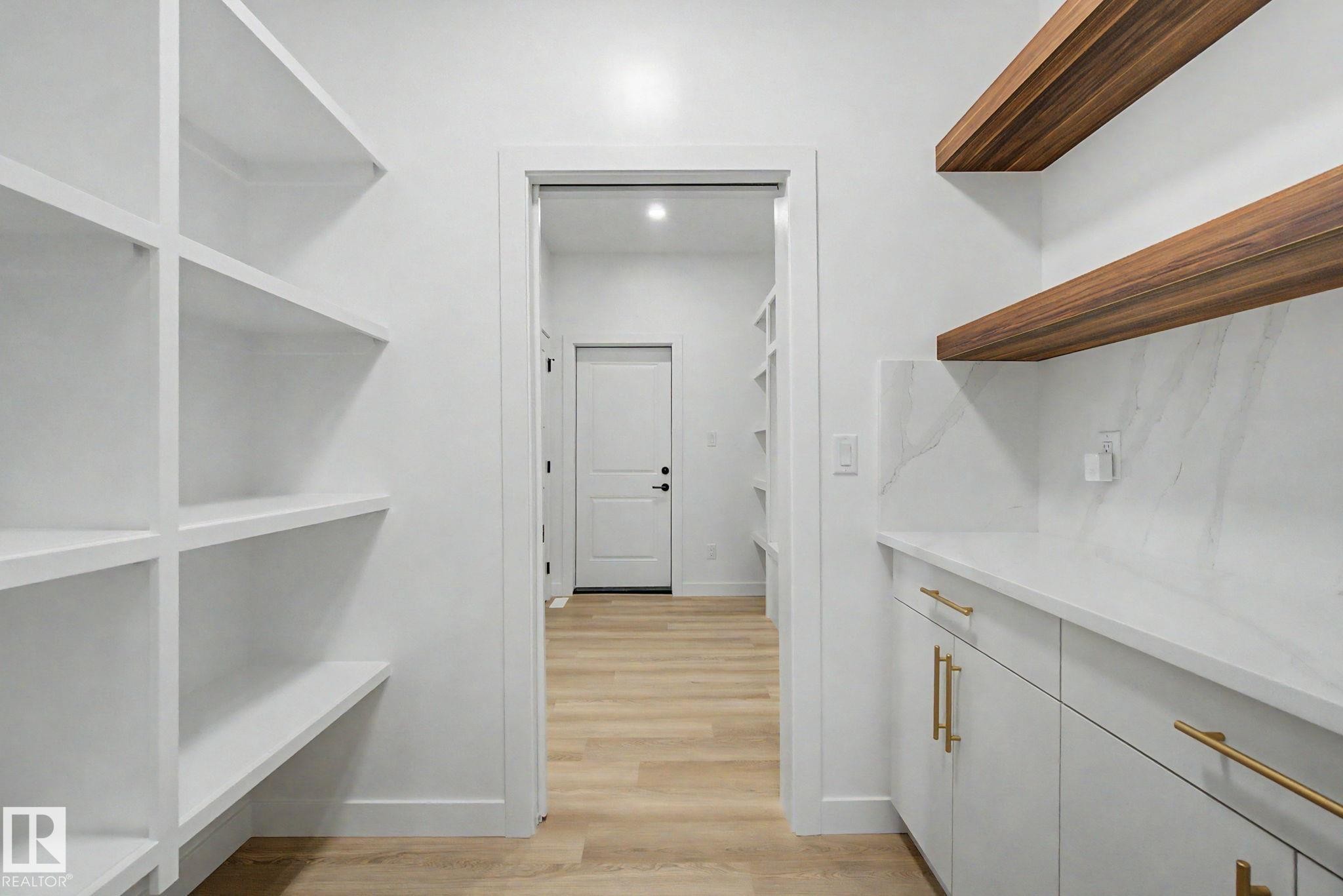 Dedicated pantry space featuring white shelving, light wood-finish flooring, white cabinetry with brass hardware, a white countertop, and wood-finish floating shelves - 4 Willow Heights Drive, Stony Plain, AB