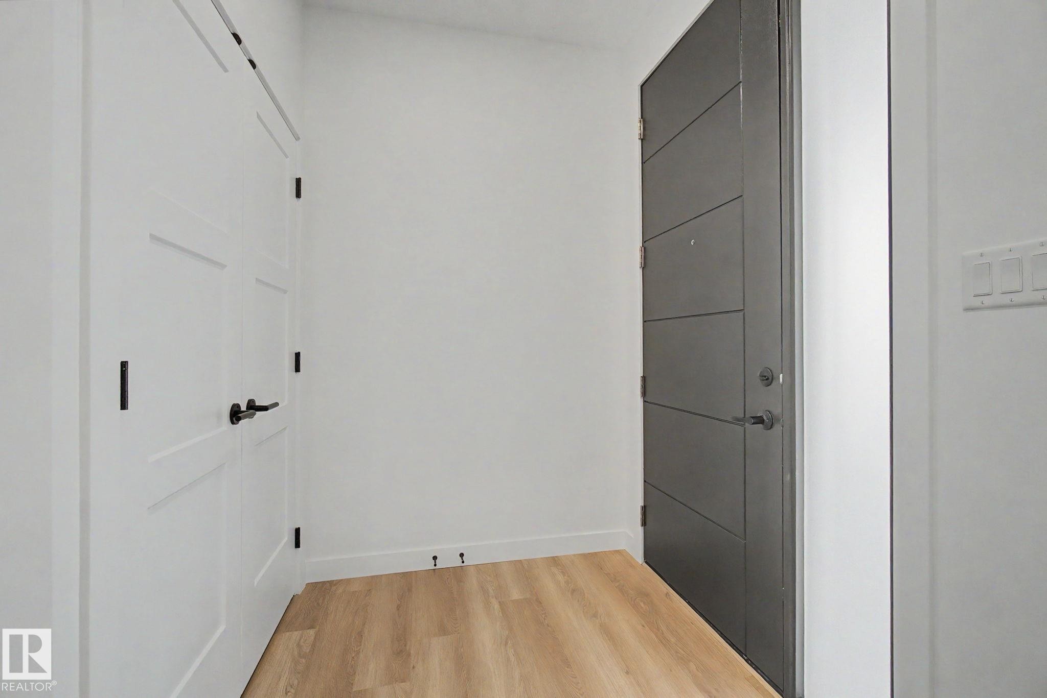 Entryway featuring a modern gray door with horizontal paneling, light wood-finish flooring, and white paneled doors with black hardware - 4 Willow Heights Drive, Stony Plain, AB