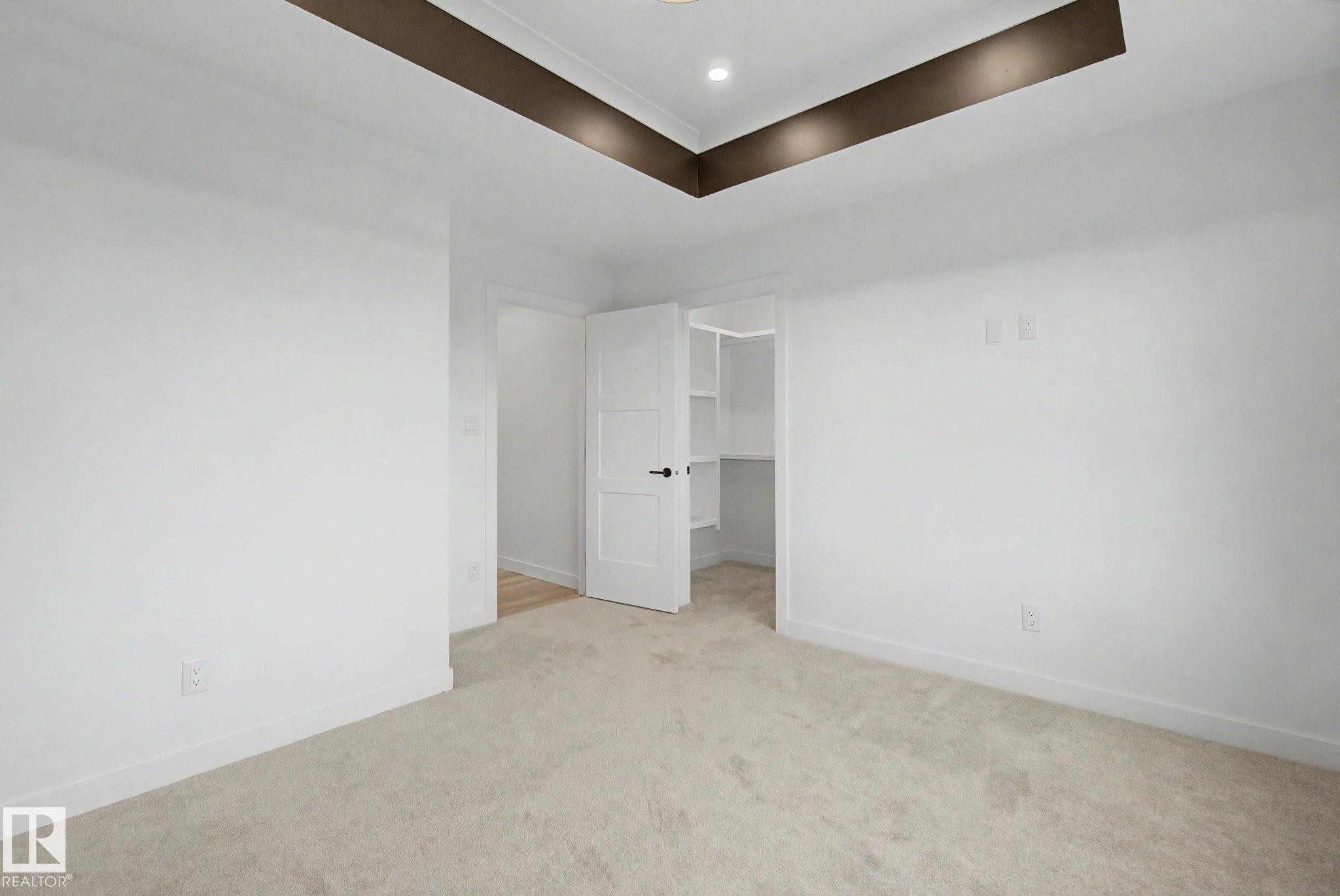 Recessed tray ceiling with integrated lighting, soft carpet flooring, white interior walls, white trim, and a white interior door with dark hardware opening to a built-in closet with shelving - 4 Willow Heights Drive, Stony Plain, AB