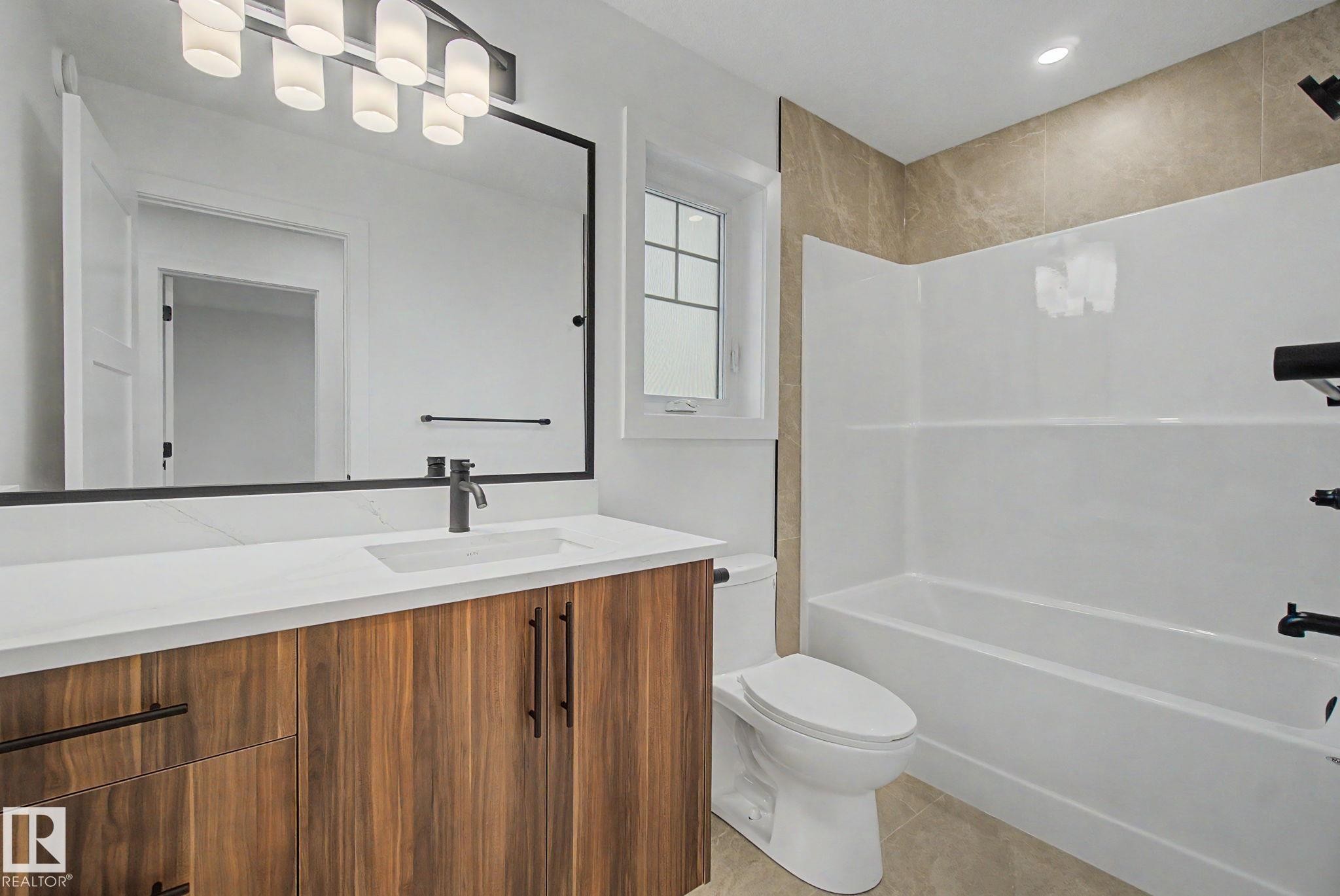 Bathroom featuring a wood-finish vanity with a white countertop and integrated sink, a large framed mirror, and a modern light fixture - 4 Willow Heights Drive, Stony Plain, AB