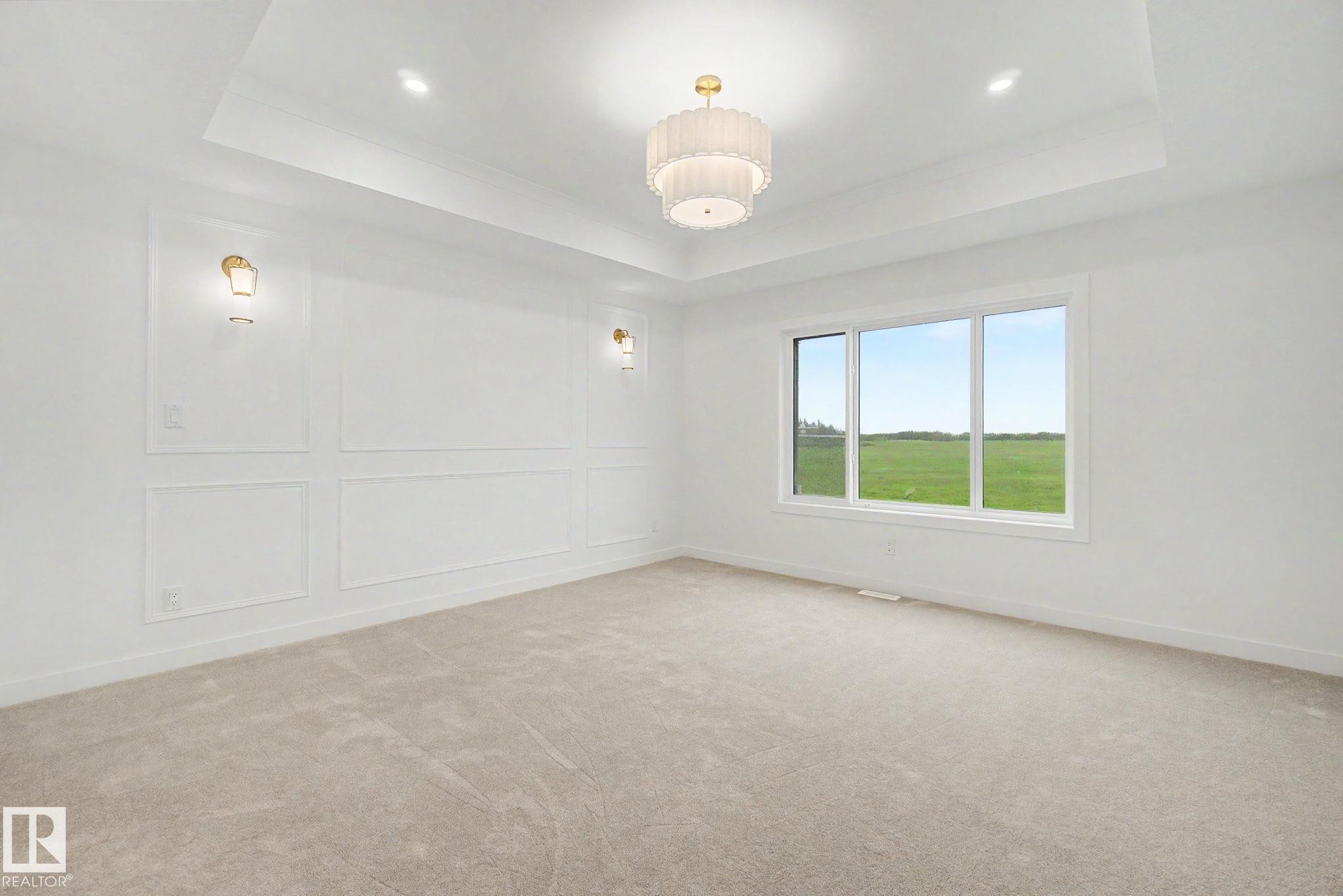 Spacious room featuring a tray ceiling with a central chandelier, decorative wall paneling, and wall sconces - 4 Willow Heights Drive, Stony Plain, AB