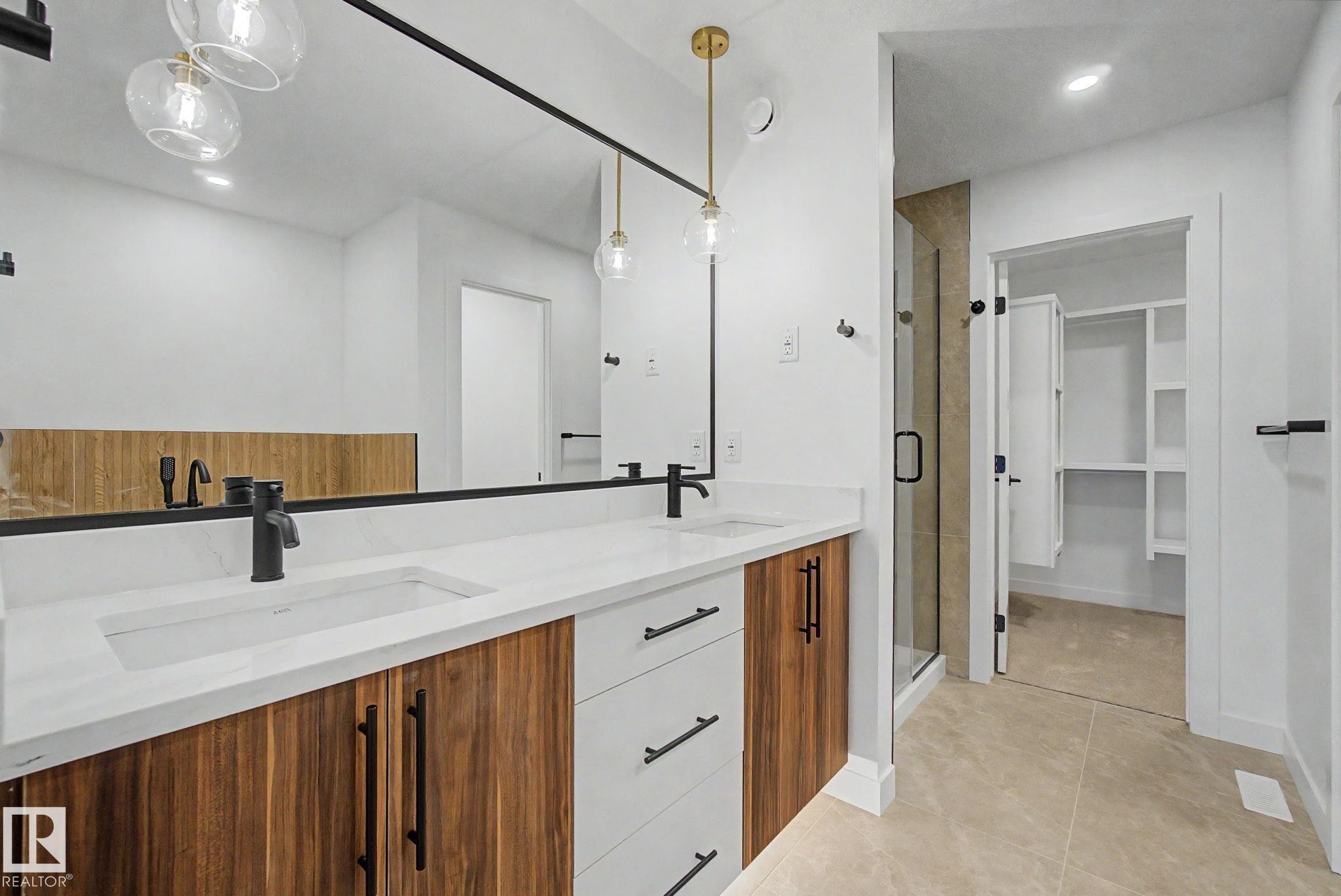 Dual vanity with integrated sinks, white countertops, wood-finish cabinetry, matte black fixtures, and a glass-enclosed shower - 4 Willow Heights Drive, Stony Plain, AB