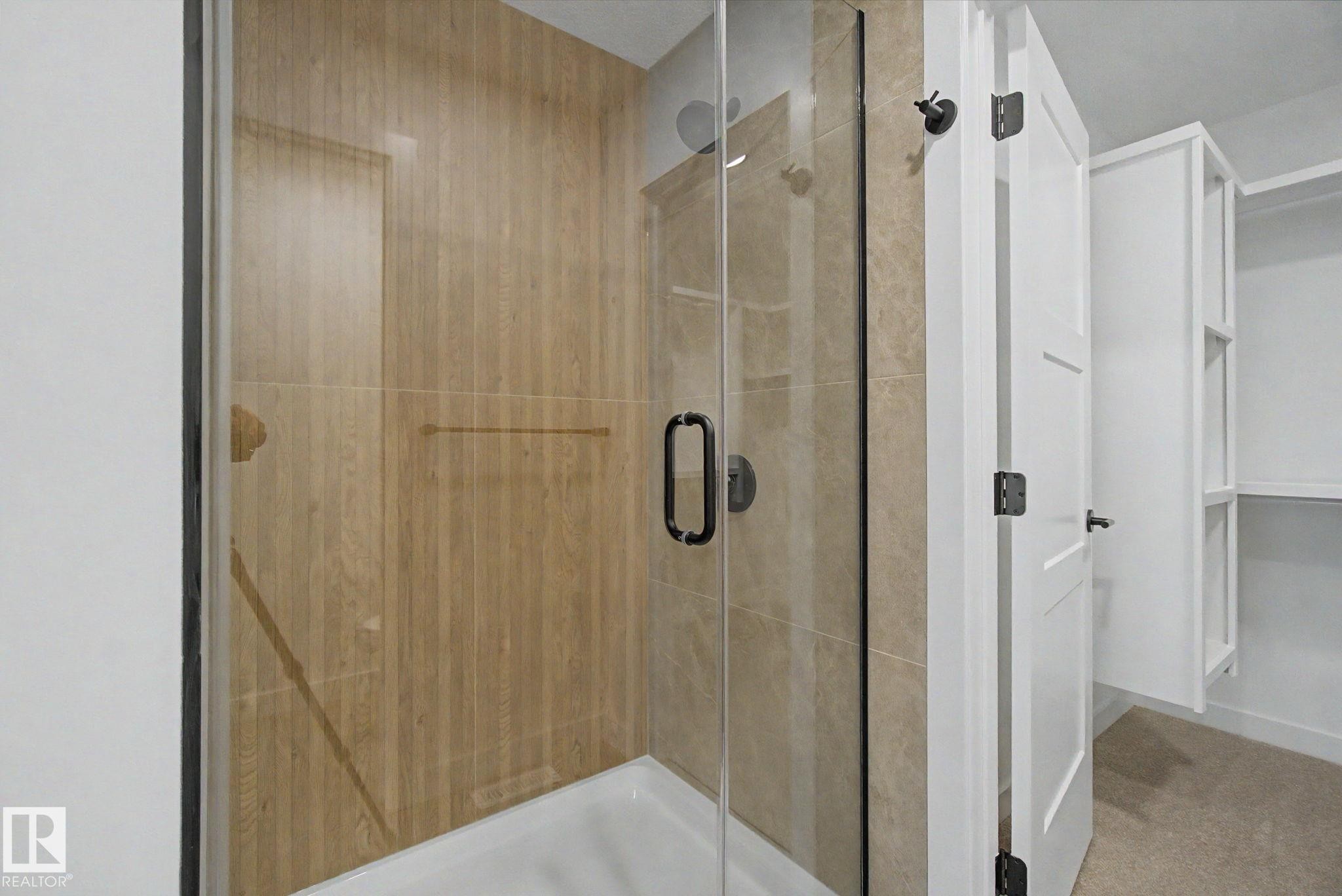 Glass-enclosed shower with wood-finish tile surround and a matte black shower head - 4 Willow Heights Drive, Stony Plain, AB